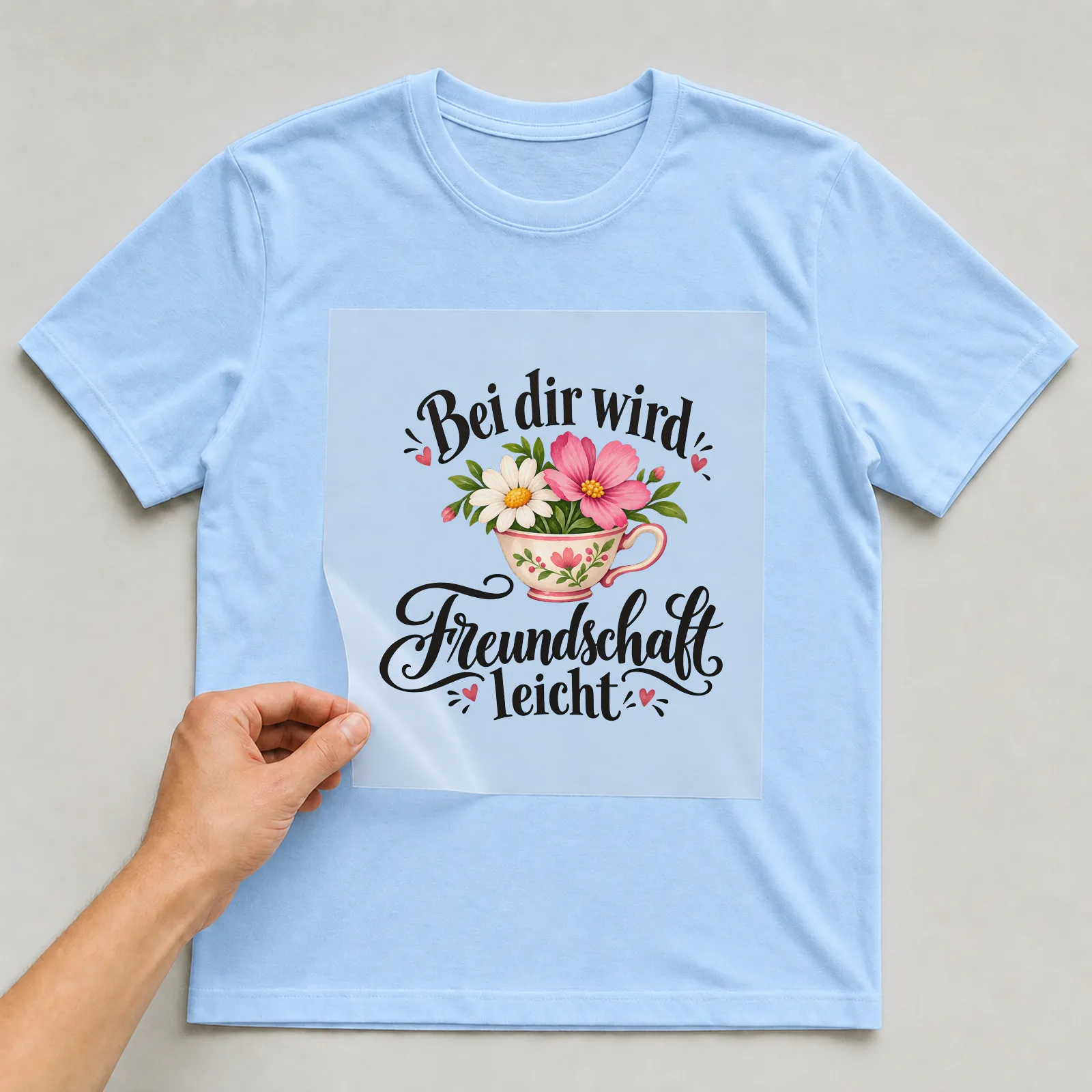 Bügelbild „Bei dir wird Freundschaft leicht“ auf hellblauem T-Shirt, Folie wird aufgelegt