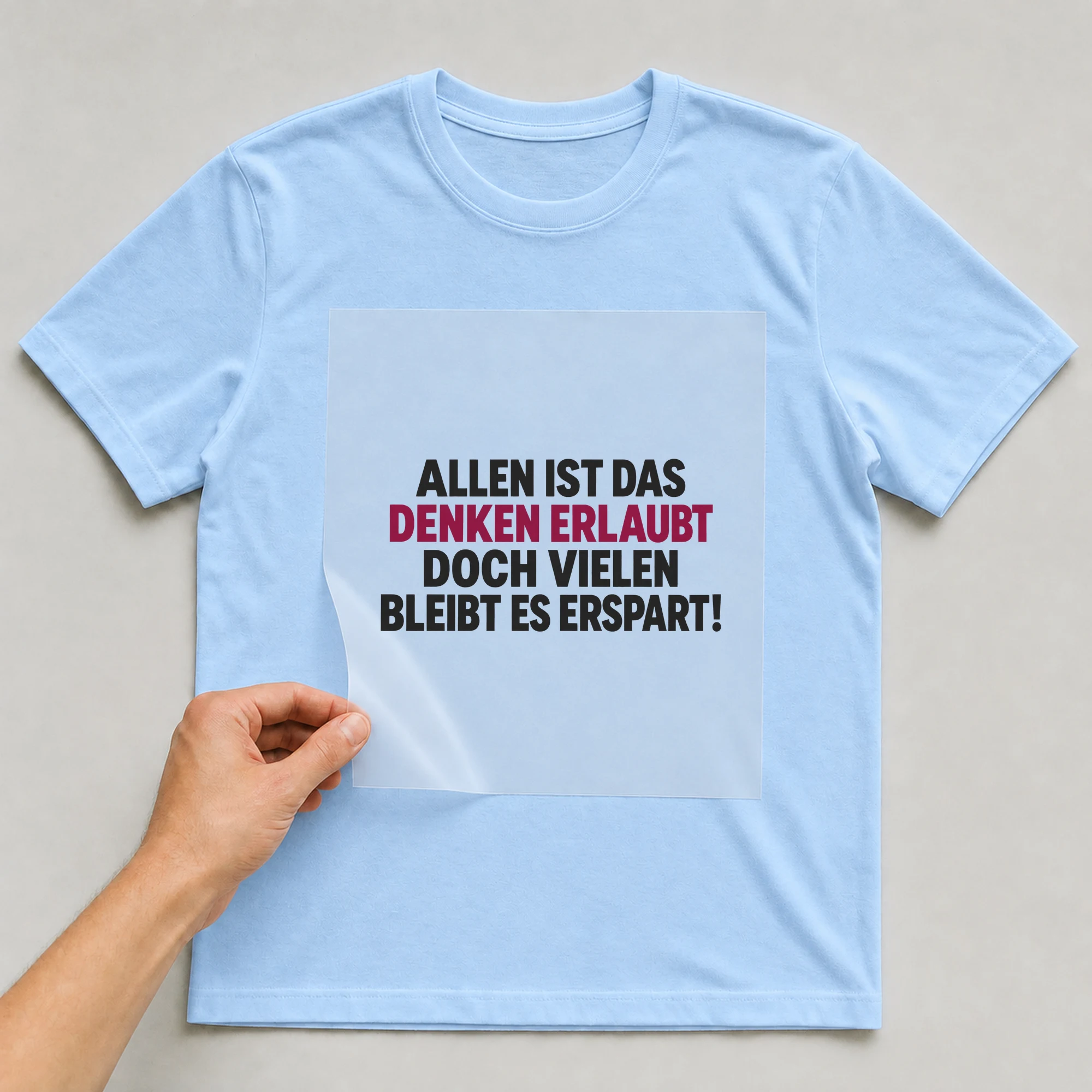 Bügelbild „Allen ist das denken erlaubt doch vielen bleibt es erspart!“ auf babyblauem T-Shirt, Folie wird aufgelegt