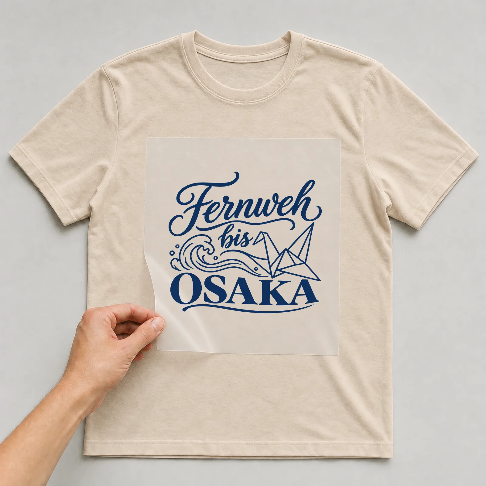 Bügelbild „Fernweh bis Osaka“ auf beigem T-Shirt, Folie wird aufgelegt