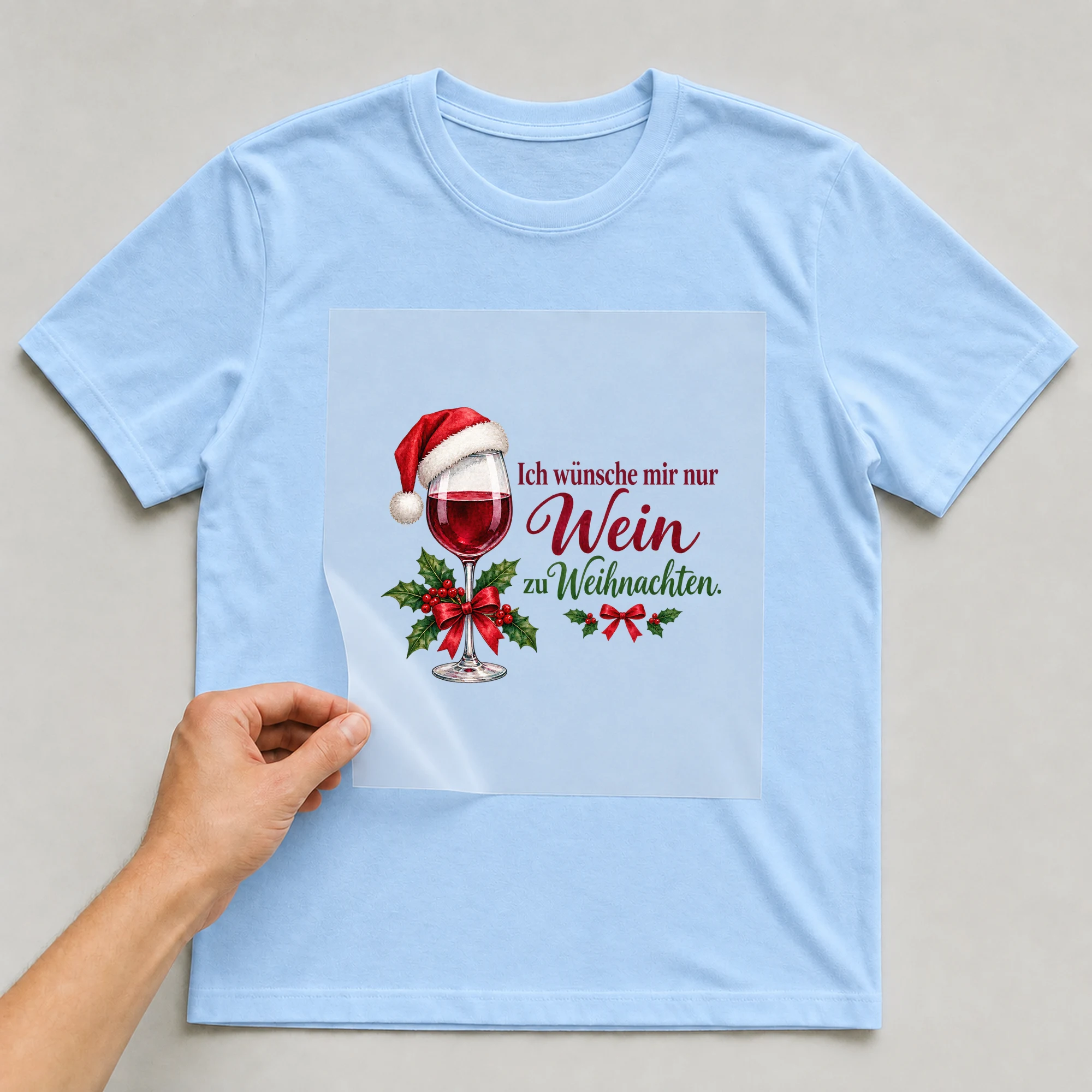 Bügelbild „Ich wünsche mir nur Wein zu Weihnachten.“ auf babyblauem T-Shirt, Folie wird aufgelegt