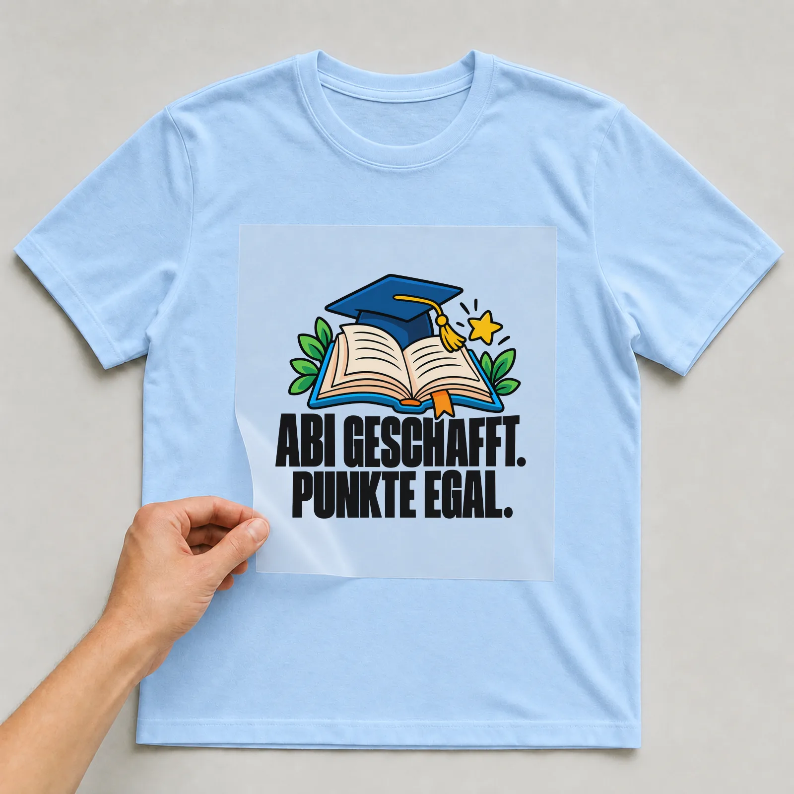 Bügelbild „Abi geschafft. Punkte egal.“ auf hellblauem T-Shirt, Folie wird aufgelegt