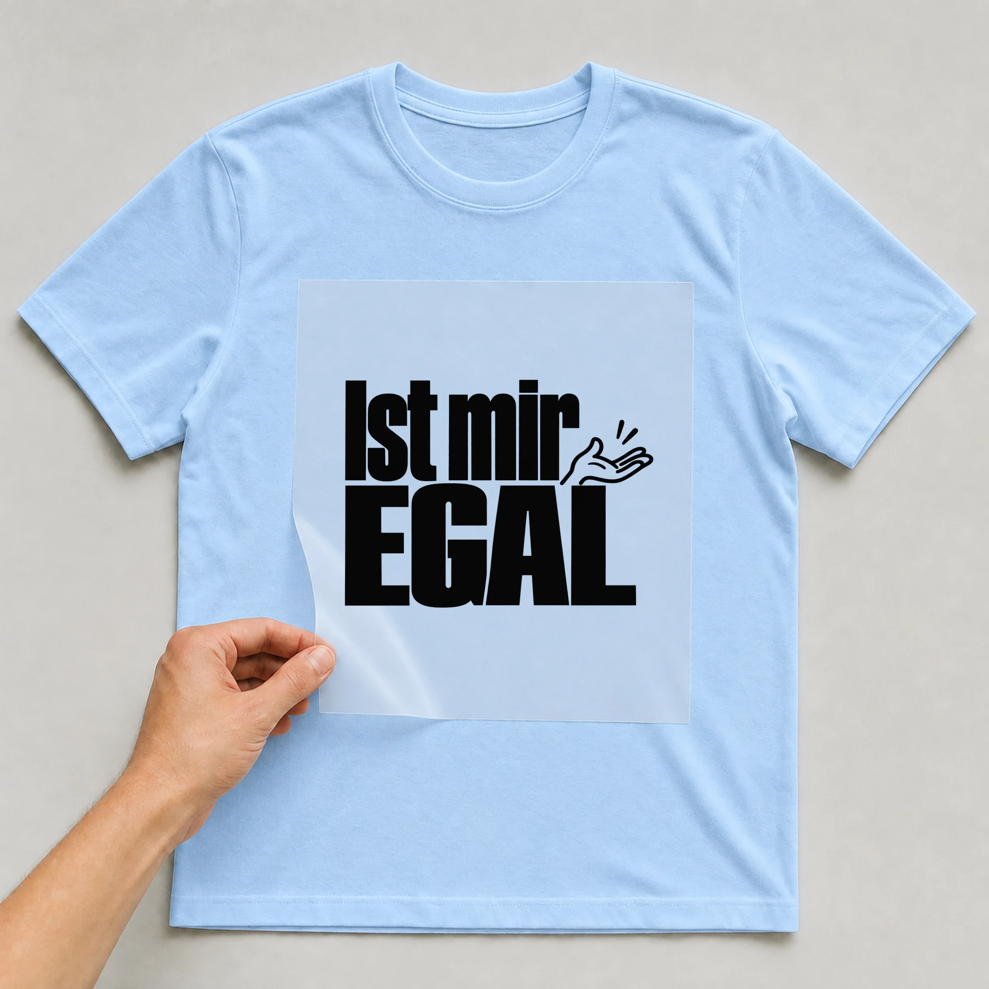 Bügelbild „Ist mir EGAL“ auf babyblauem T-Shirt, Folie wird aufgelegt