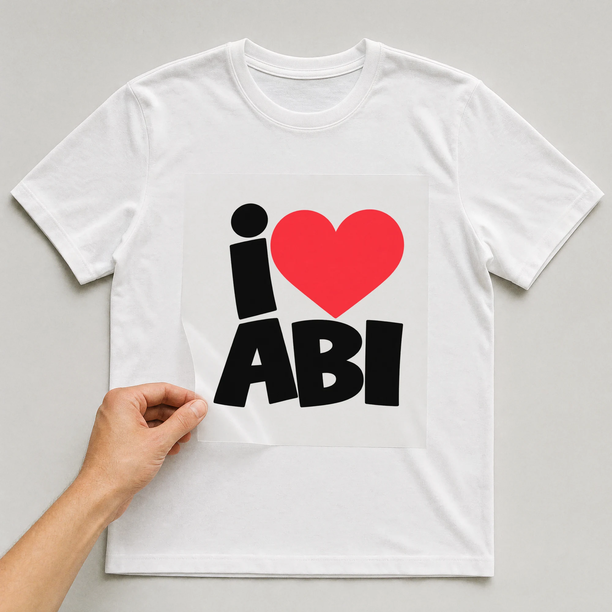 Bügelbild „i Herz ABI“ auf weißem T-Shirt, Folie wird aufgelegt