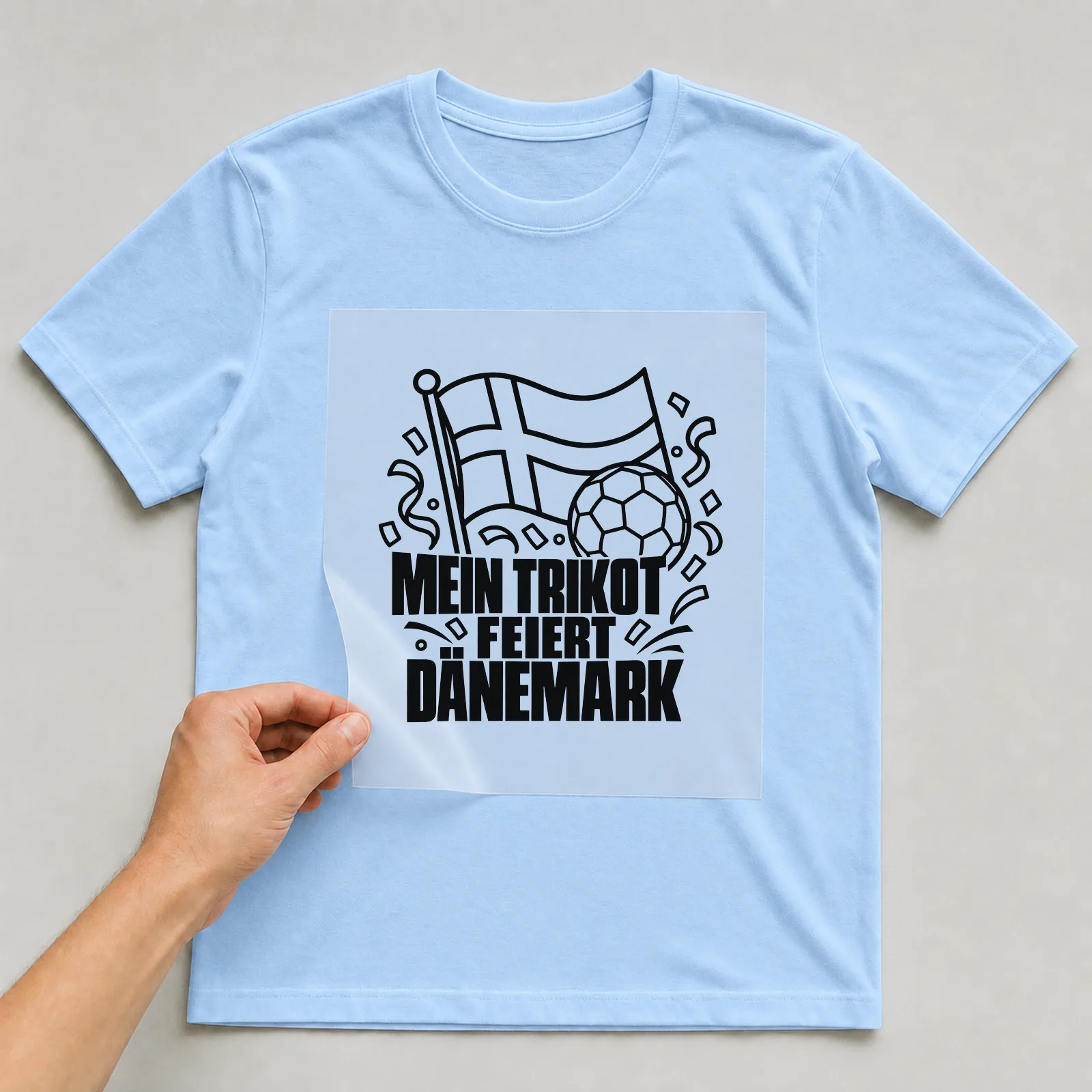 Bügelbild „Mein Trikot feiert Dänemark“ auf hellblauem T-Shirt, Folie wird aufgelegt