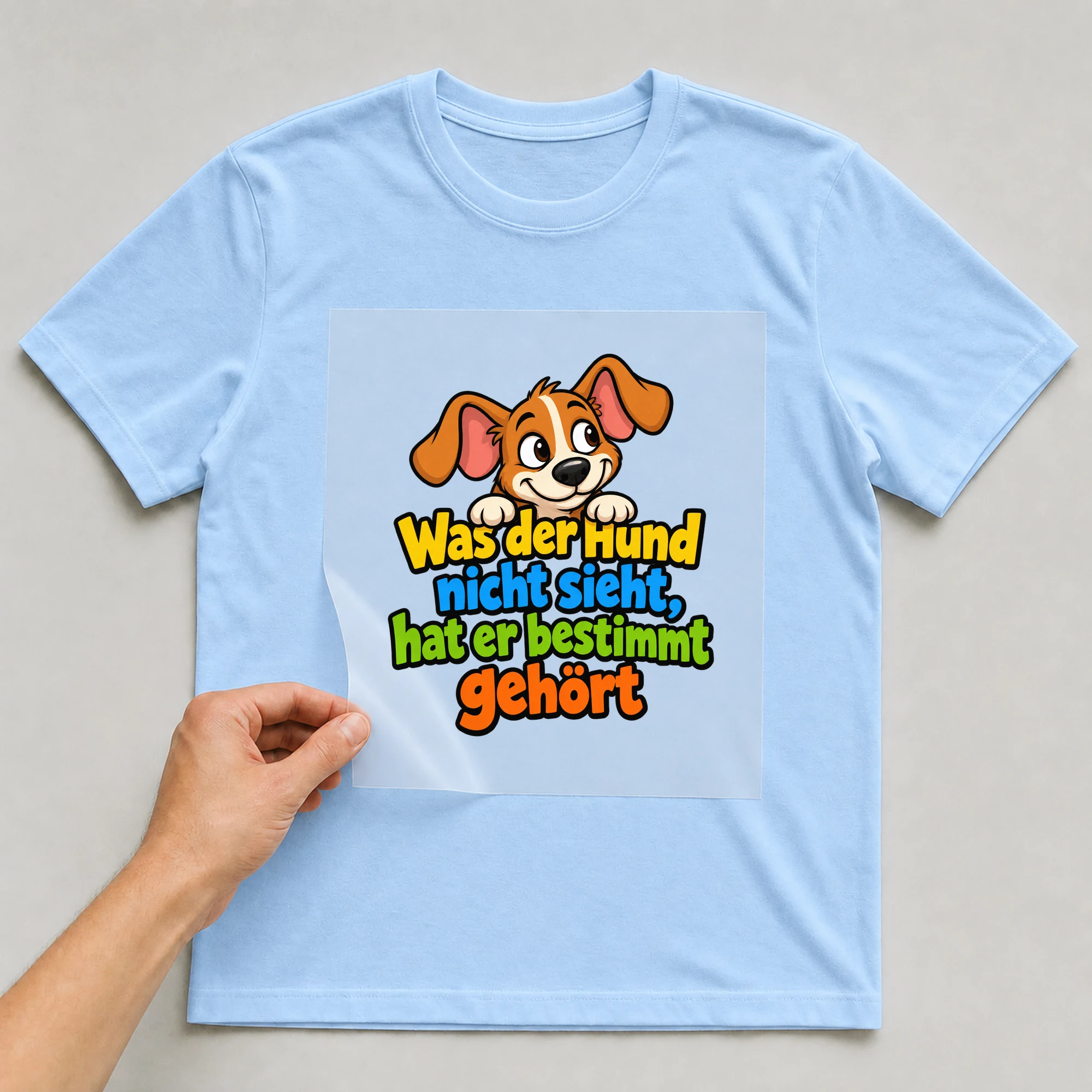 Bügelbild „Was der Hund nicht sieht, hat er bestimmt gehört“ auf babyblauem T-Shirt, Folie wird aufgelegt