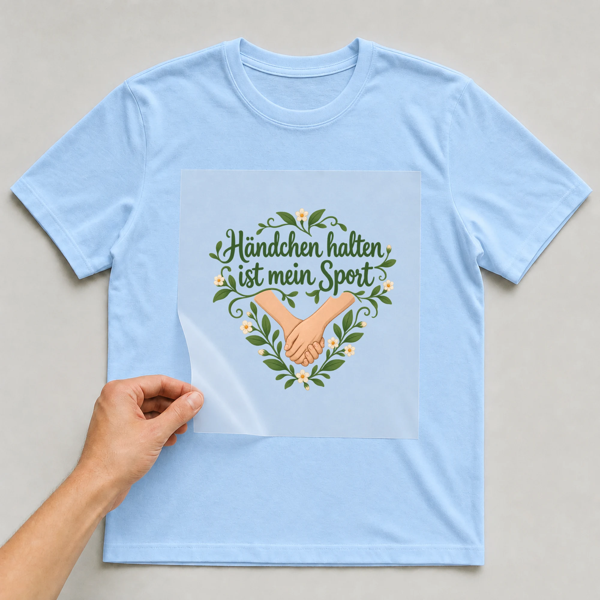 Bügelbild „Händchen halten ist mein Sport“ auf babyblauem T-Shirt, Folie wird aufgelegt