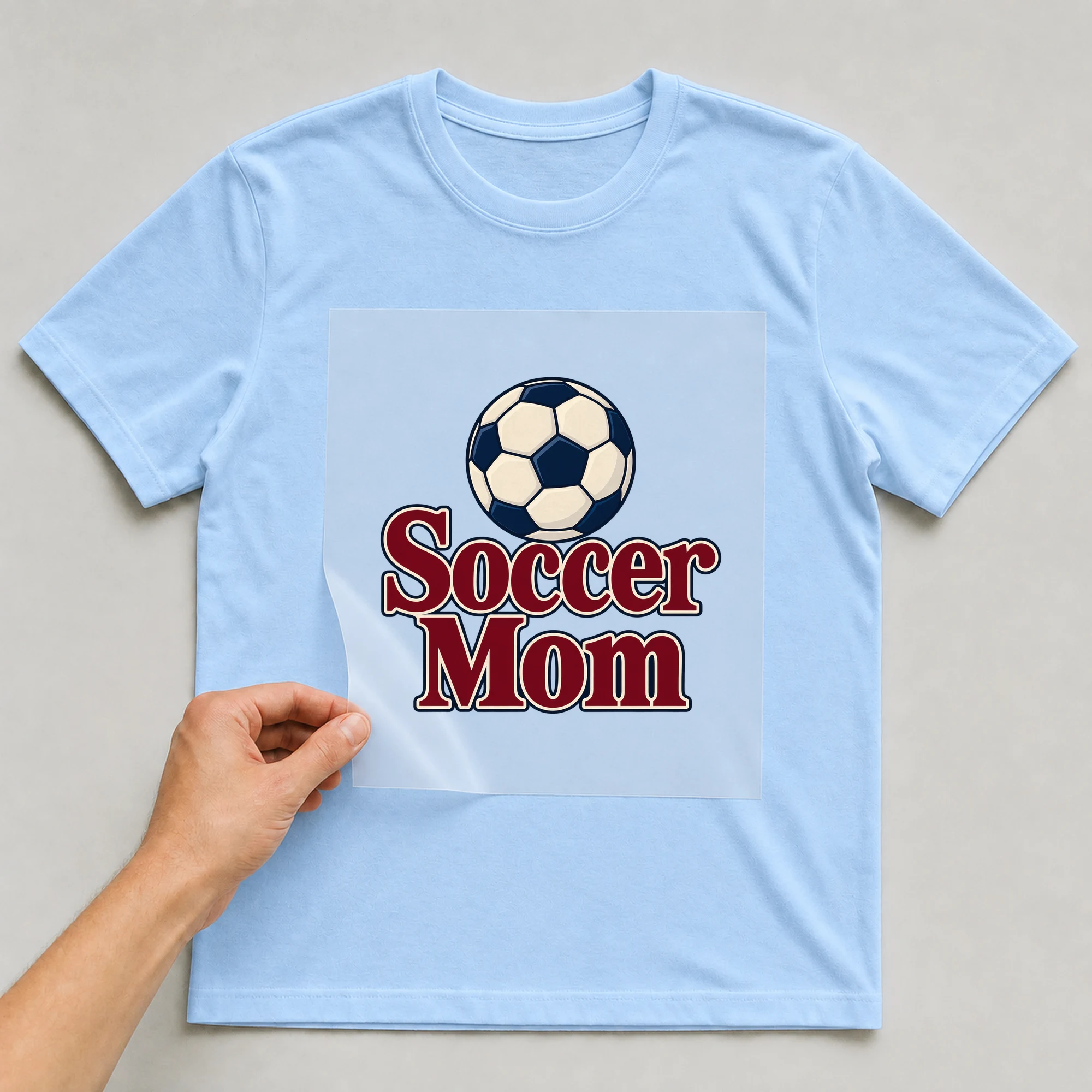 Bügelbild „Soccer Mom“ auf babyblauem T-Shirt, Folie wird aufgelegt