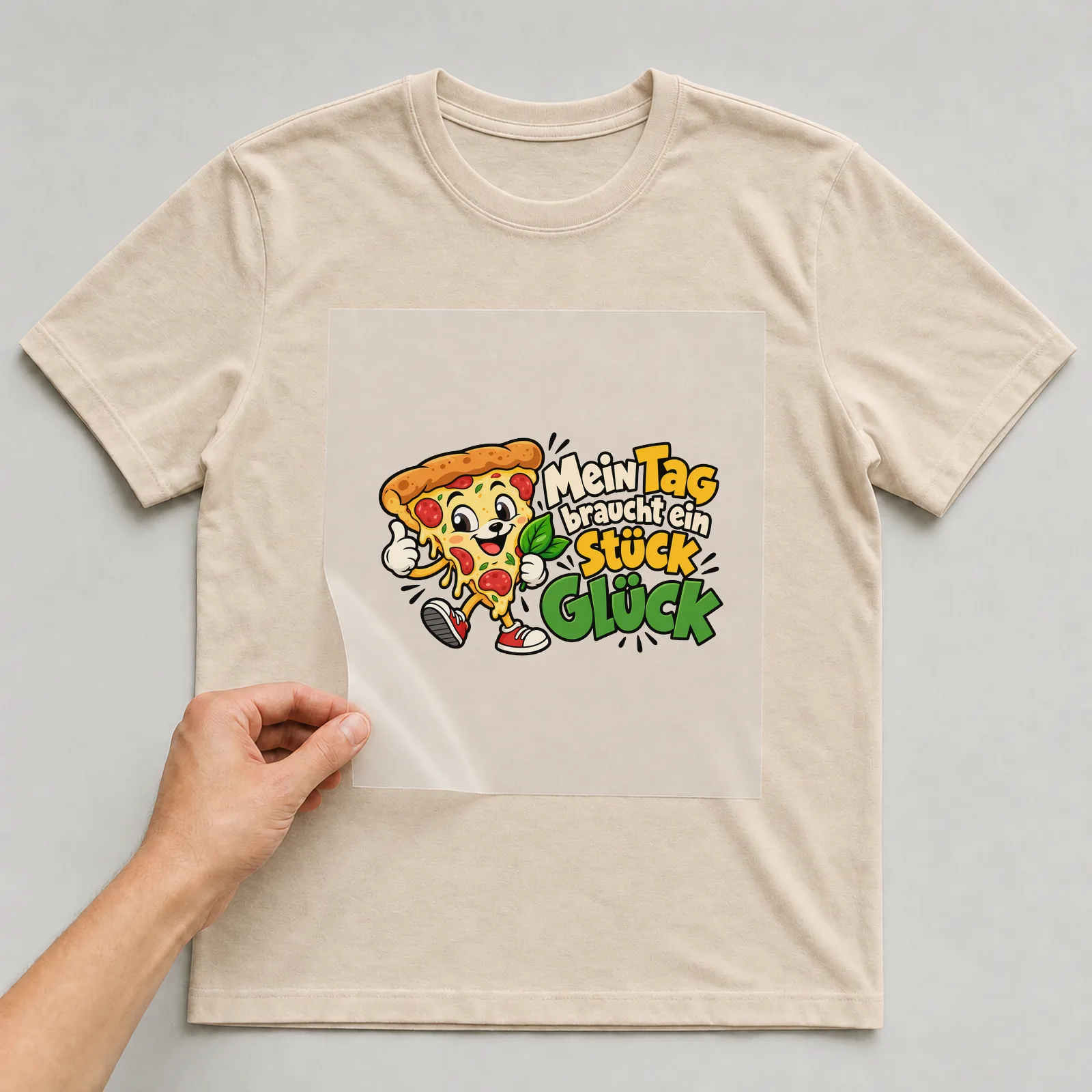Bügelbild „Mein Tag braucht ein Stück Glück“ auf beigem T-Shirt, Folie wird aufgelegt