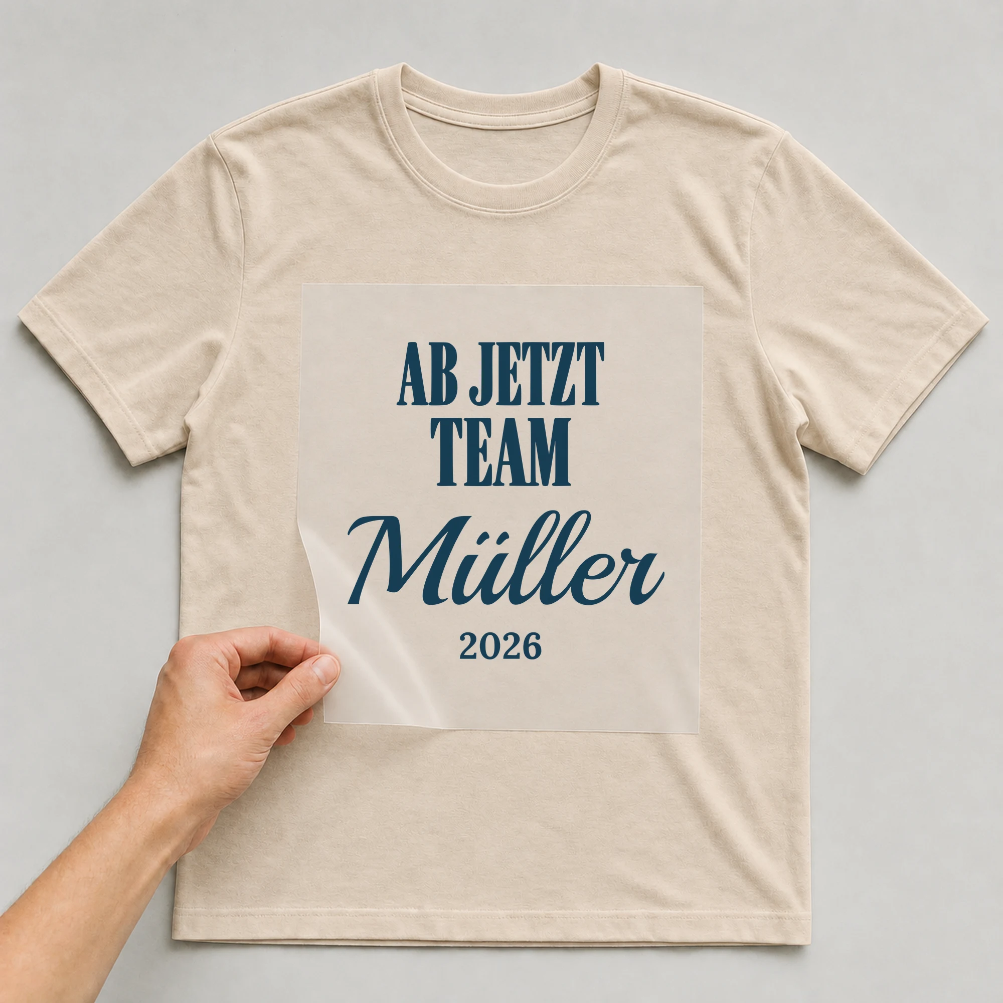 Bügelbild Ab jetzt Team mit Nachname und Jahr auf beigem T-Shirt, Folie wird aufgelegt