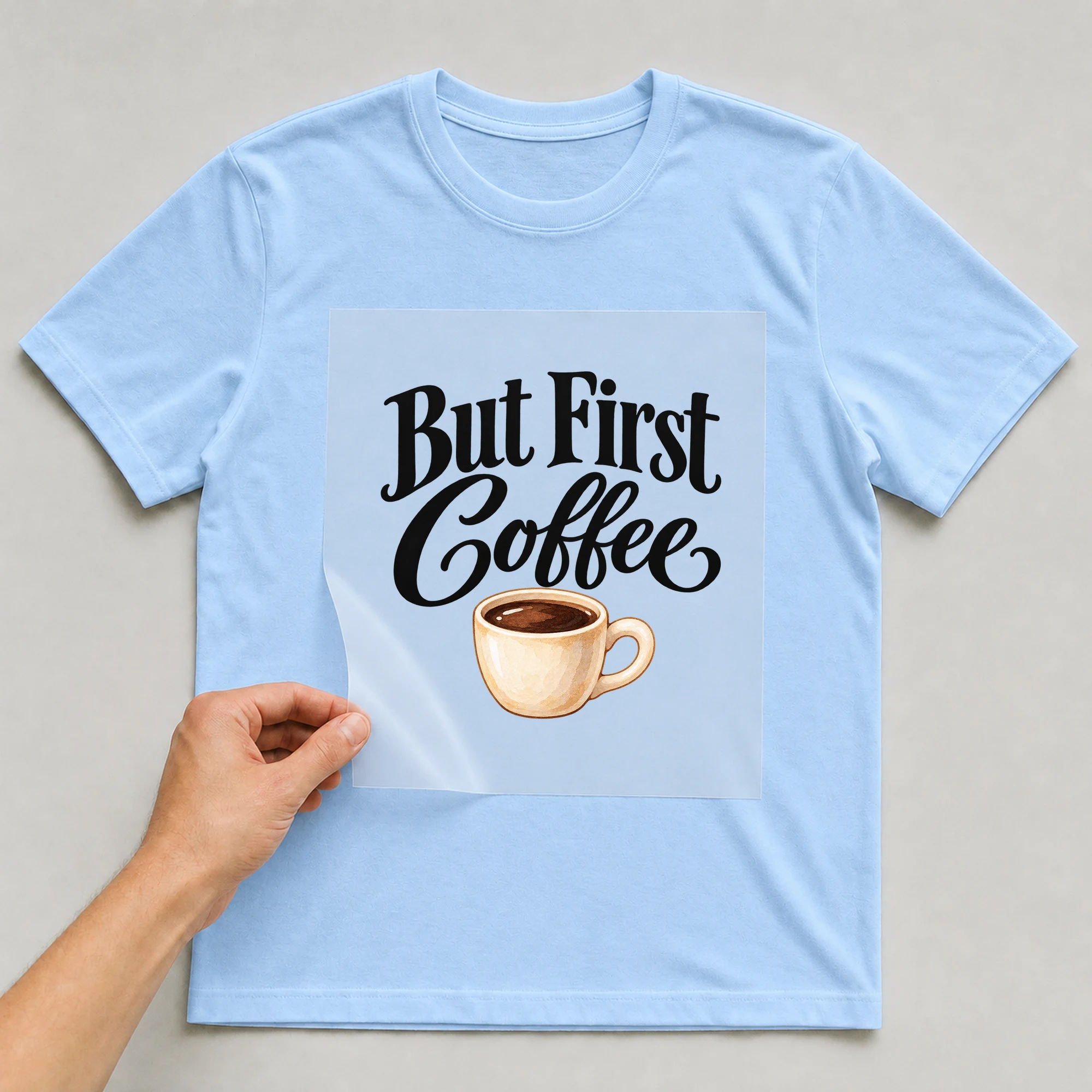 Bügelbild „But First Coffee“ auf babyblauem T-Shirt, Folie wird aufgelegt