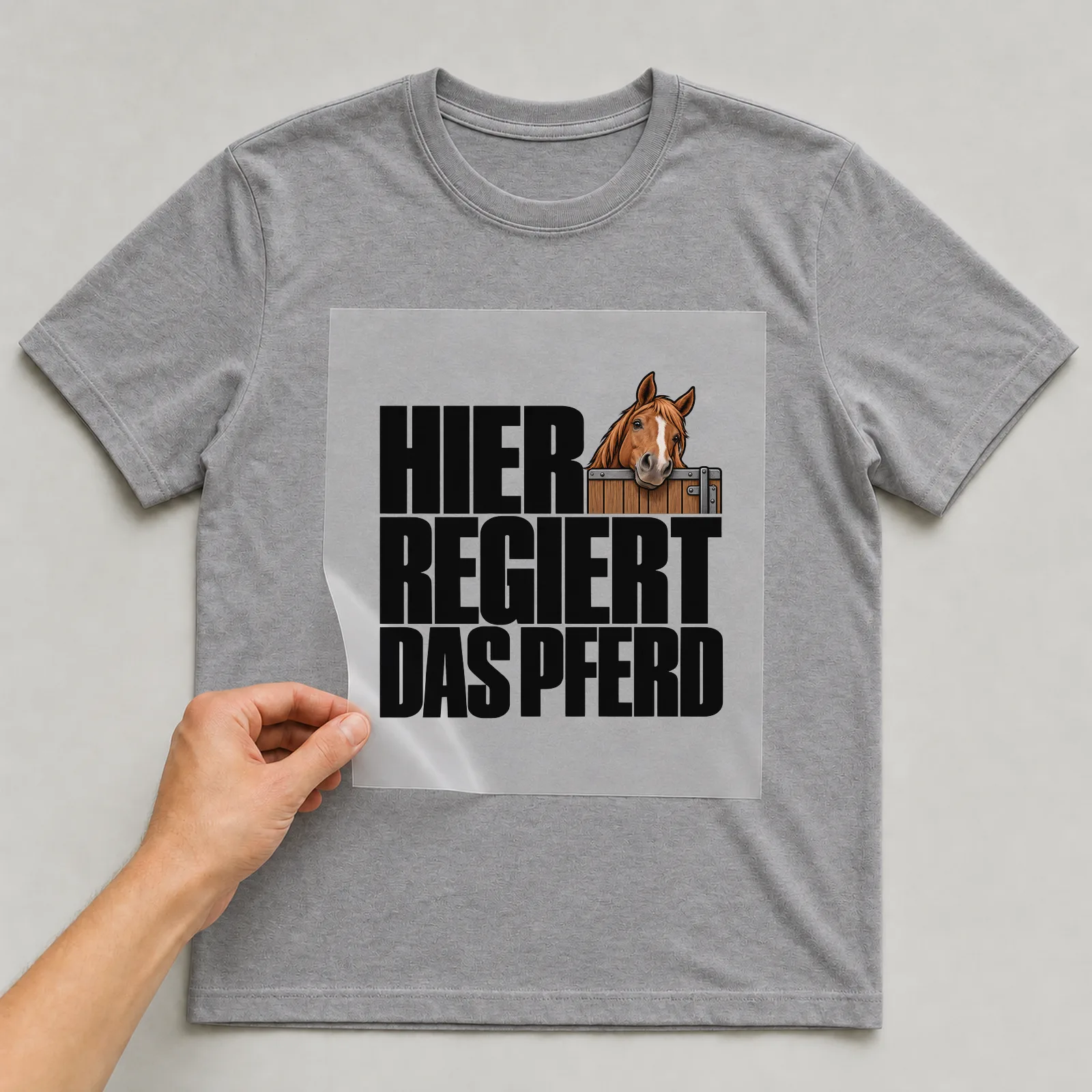 Bügelbild „Hier regiert das Pferd“ auf grauem T-Shirt, Folie wird aufgelegt