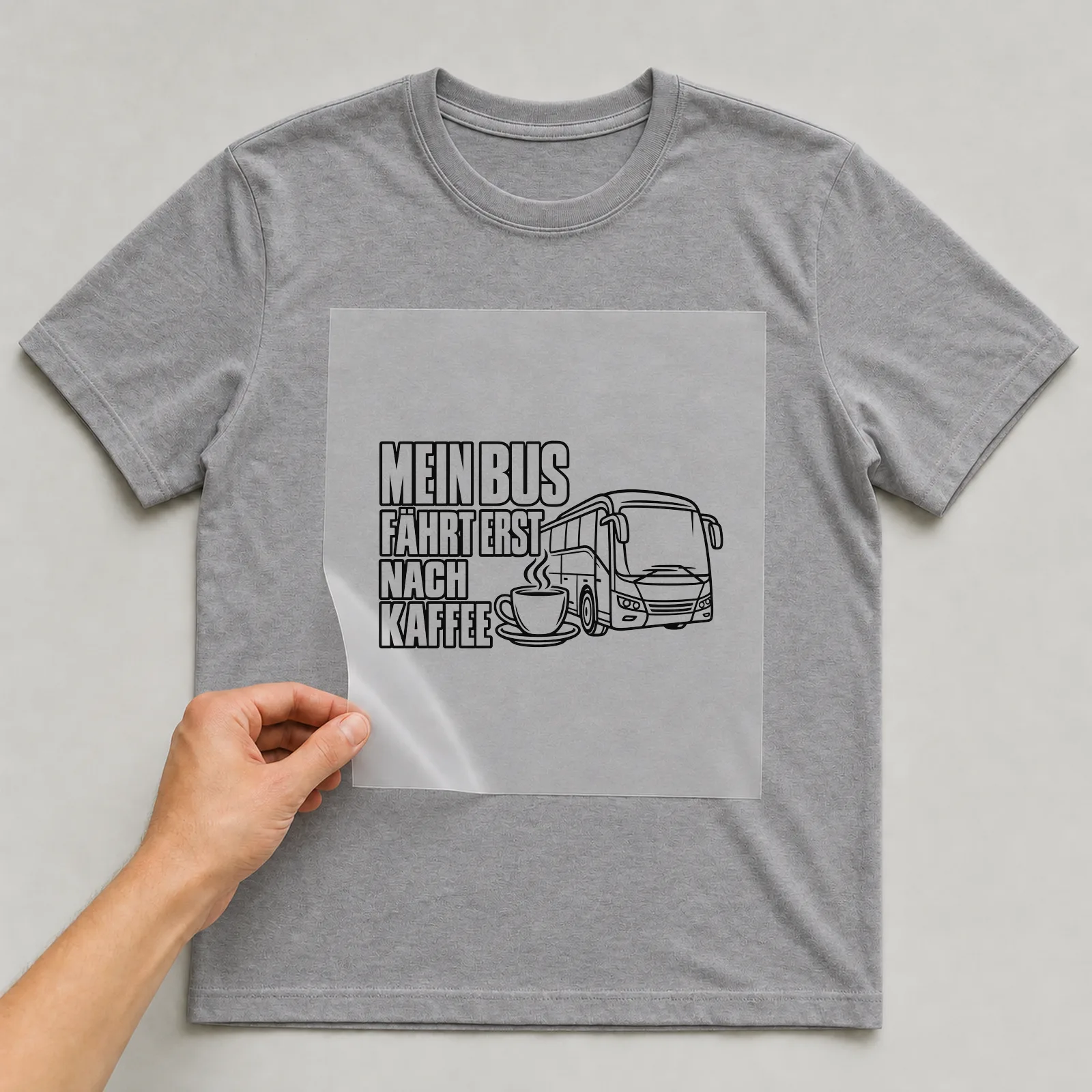 Bügelbild „Mein Bus fährt erst nach Kaffee“ auf grauem T-Shirt, Folie wird aufgelegt