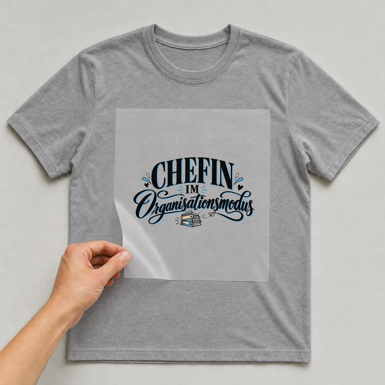 Bügelbild „Chefin im Organisationsmodus“ auf grauem T-Shirt, Folie wird aufgelegt
