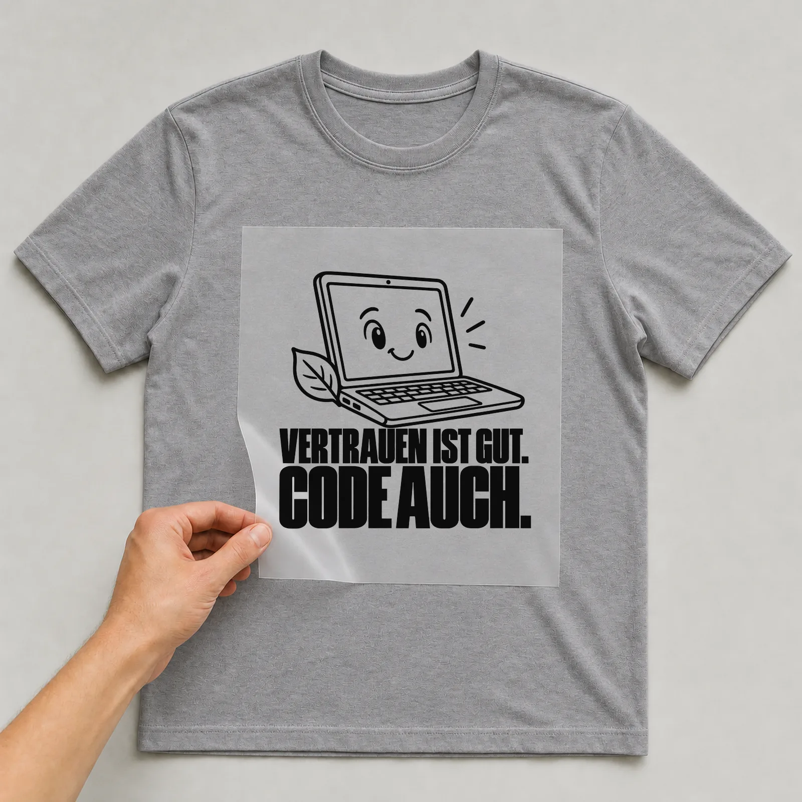 Bügelbild „Vertrauen ist gut. Code auch.“ auf grauem T-Shirt, Folie wird aufgelegt