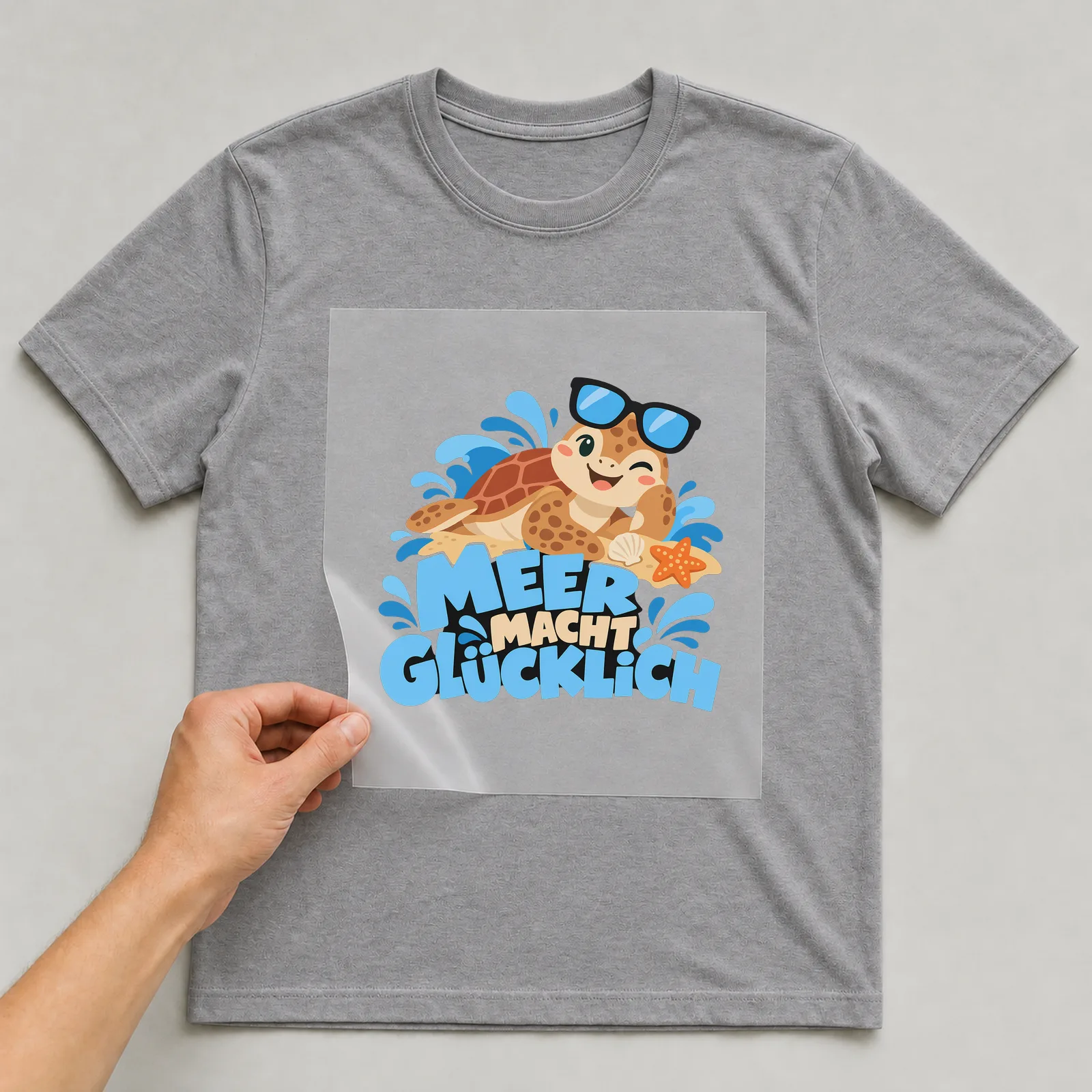 Bügelbild „Meer macht glücklich“ (organischen Formen) auf grauem T-Shirt, Folie wird aufgelegt