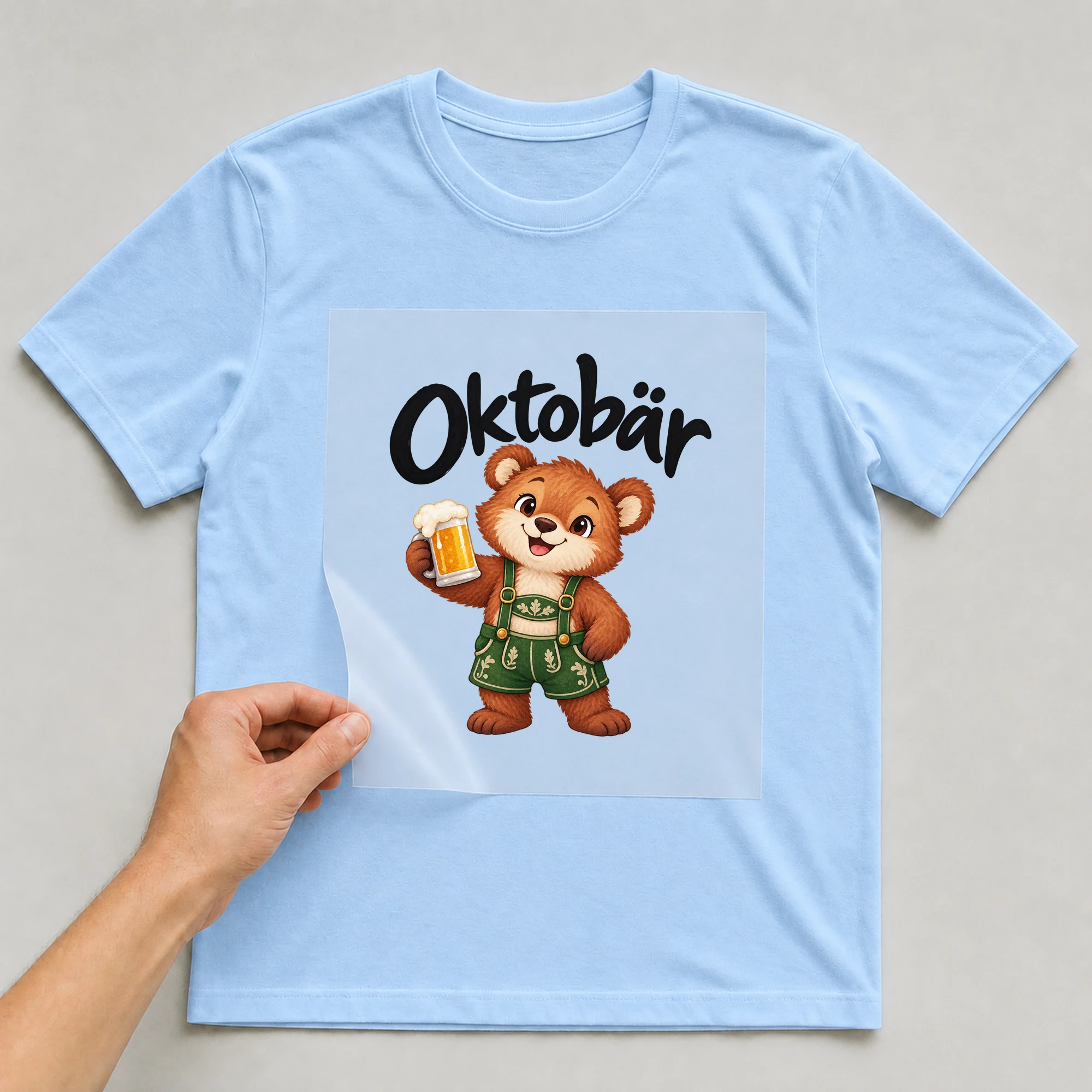 Bügelbild „Oktobär“ auf babyblauem T-Shirt, Folie wird aufgelegt