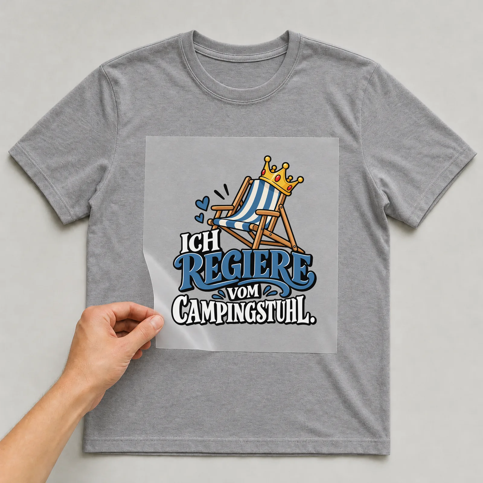 Bügelbild „Ich regiere vom Campingstuhl“ auf grauem T-Shirt, Folie wird aufgelegt