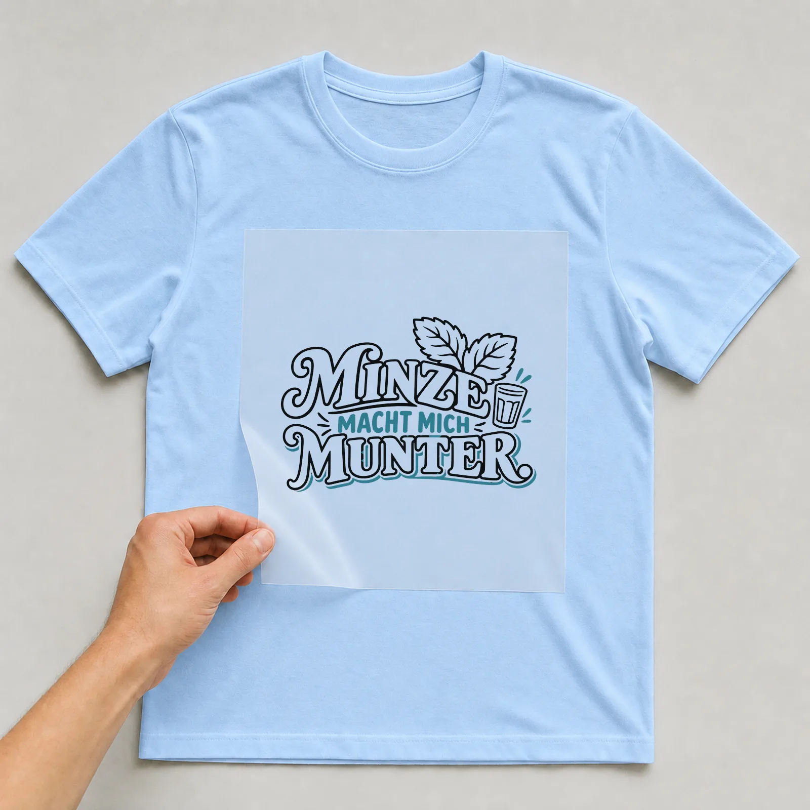 Bügelbild „Minze macht mich munter“ auf hellblauem T-Shirt, Folie wird aufgelegt