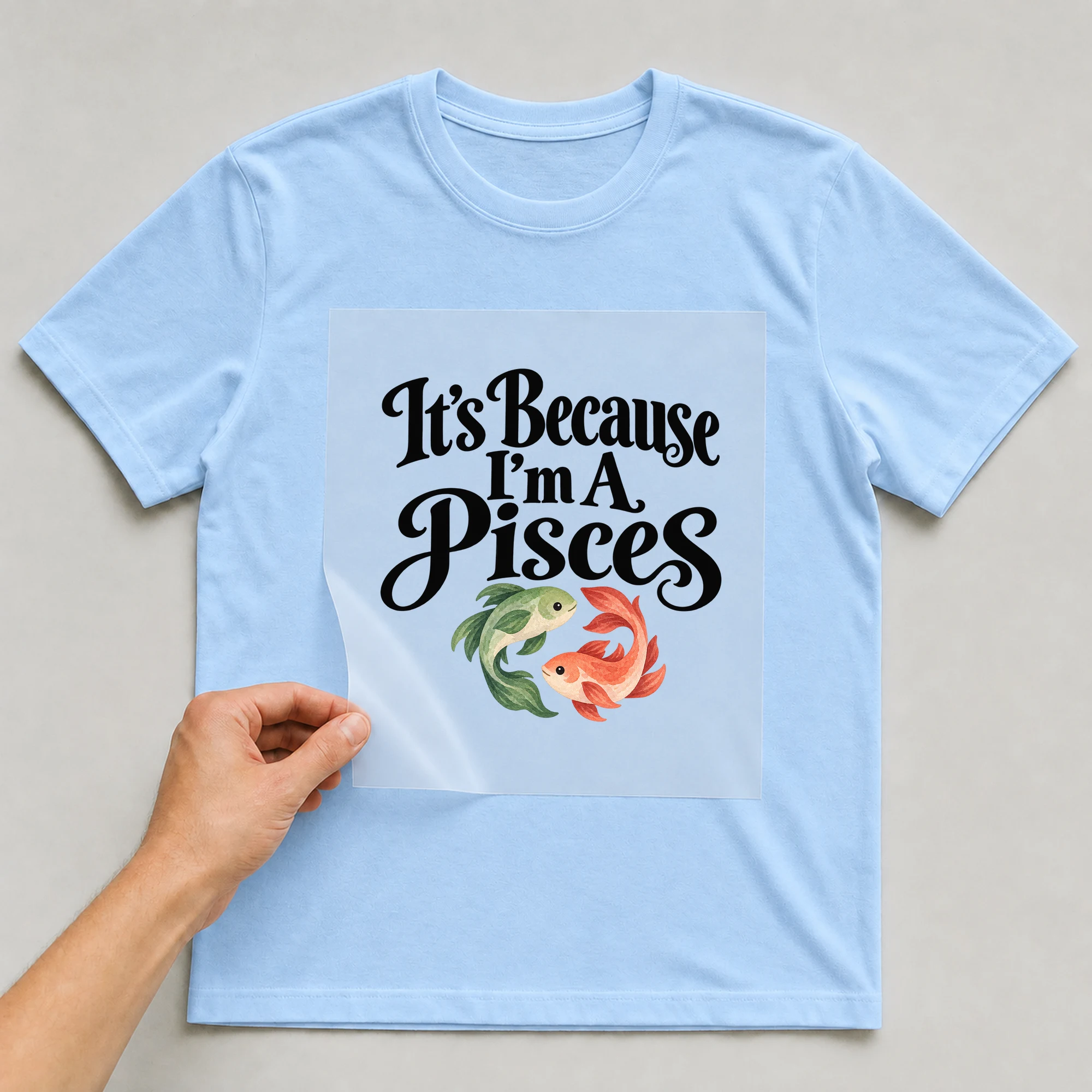 Bügelbild „It's Because I'm A Pisces“ auf babyblauem T-Shirt, Folie wird aufgelegt