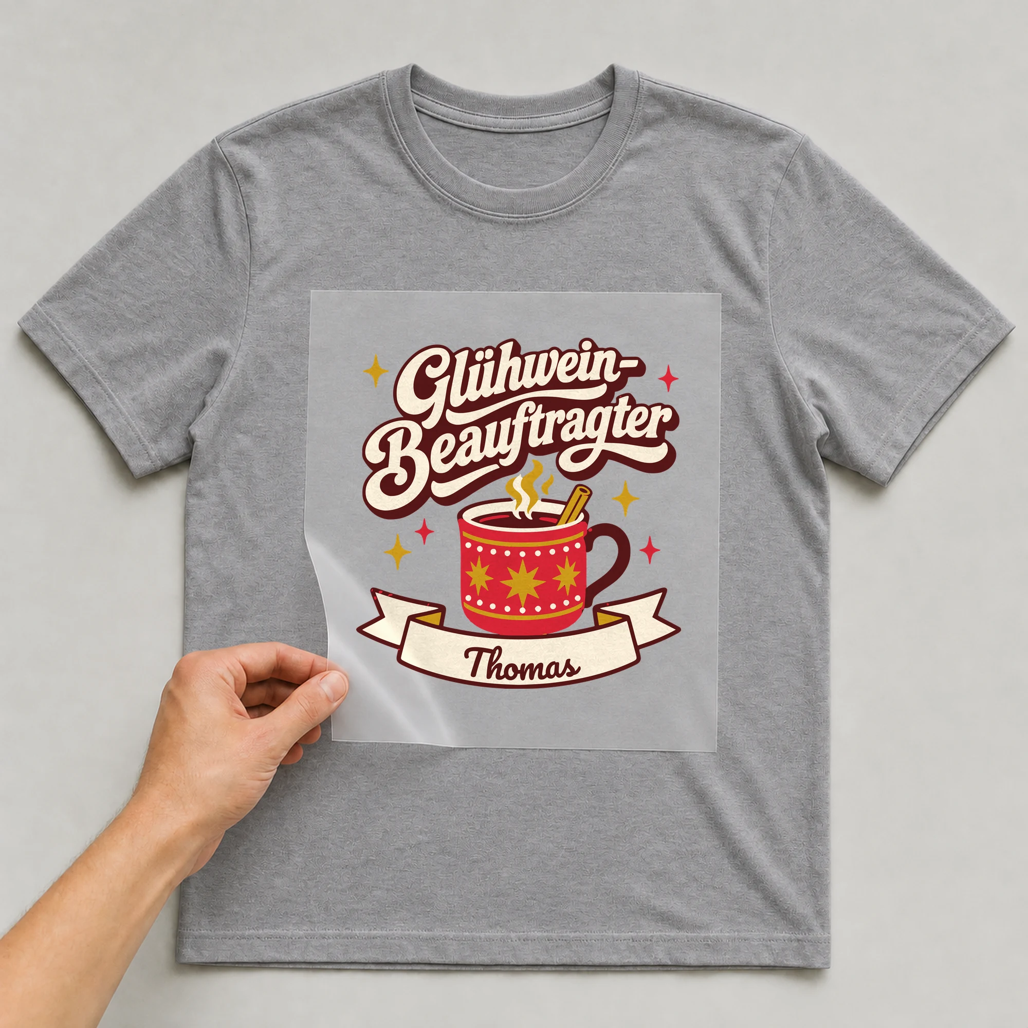 Bügelbild Glühwein-Beauftragter mit Name auf grauem T-Shirt, Folie wird aufgelegt