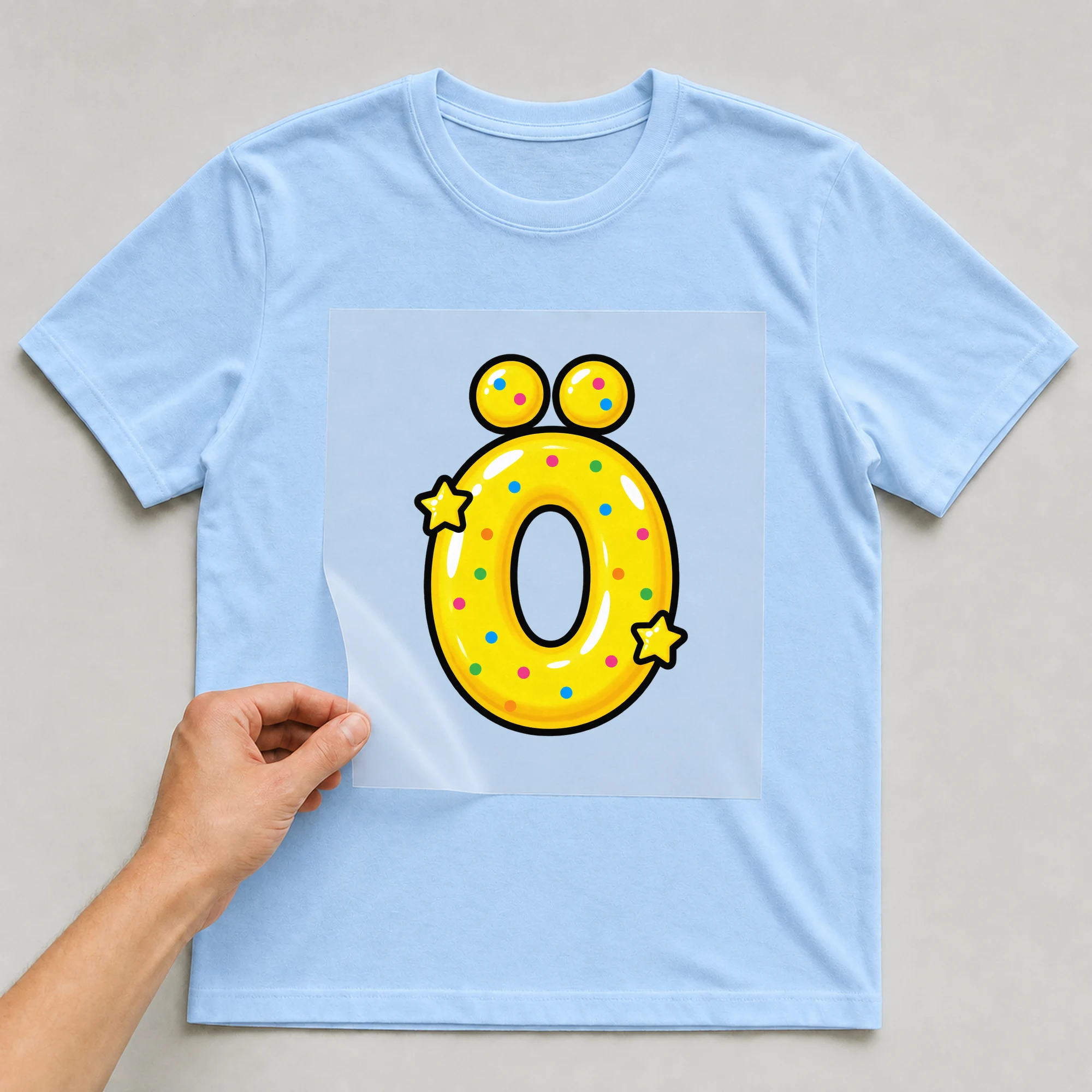 Bügelbild „Buchstabe Ö im Comic-Ballon-Stil“ auf babyblauem T-Shirt, Folie wird aufgelegt