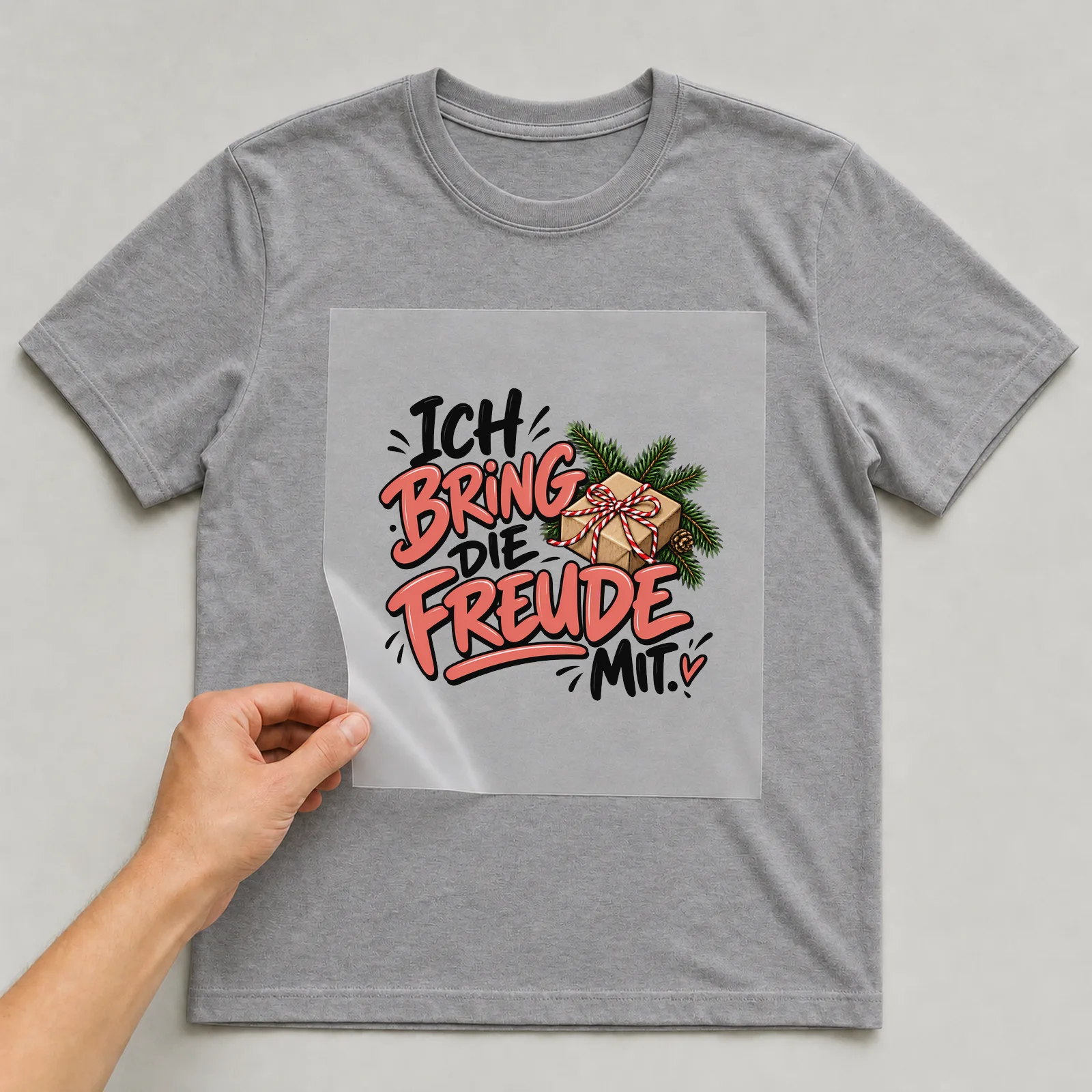 Bügelbild „Ich bring die Freude mit“ auf grauem T-Shirt, Folie wird aufgelegt