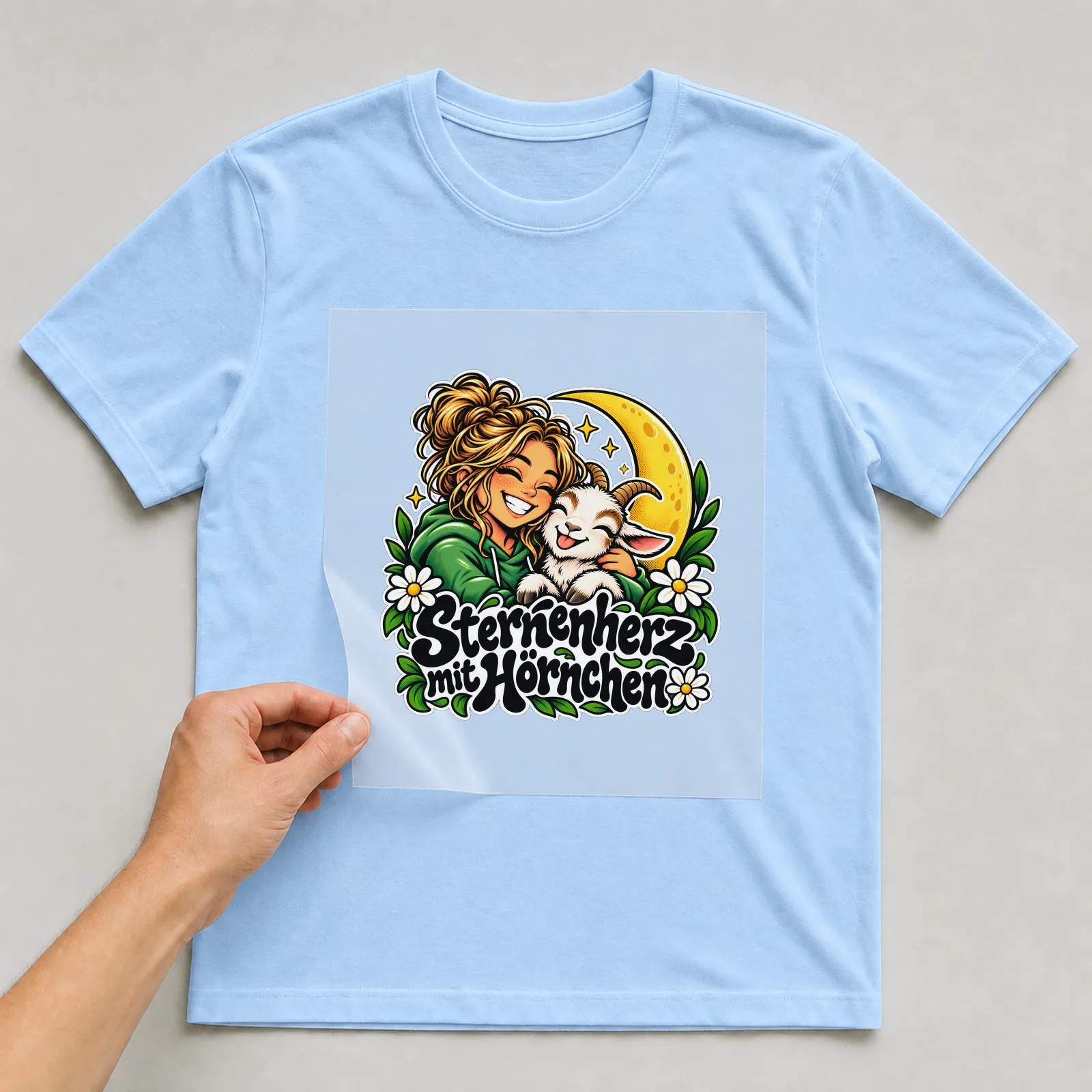 Bügelbild „Sternenherz mit Hörnchen“ auf hellblauem T-Shirt, Folie wird aufgelegt