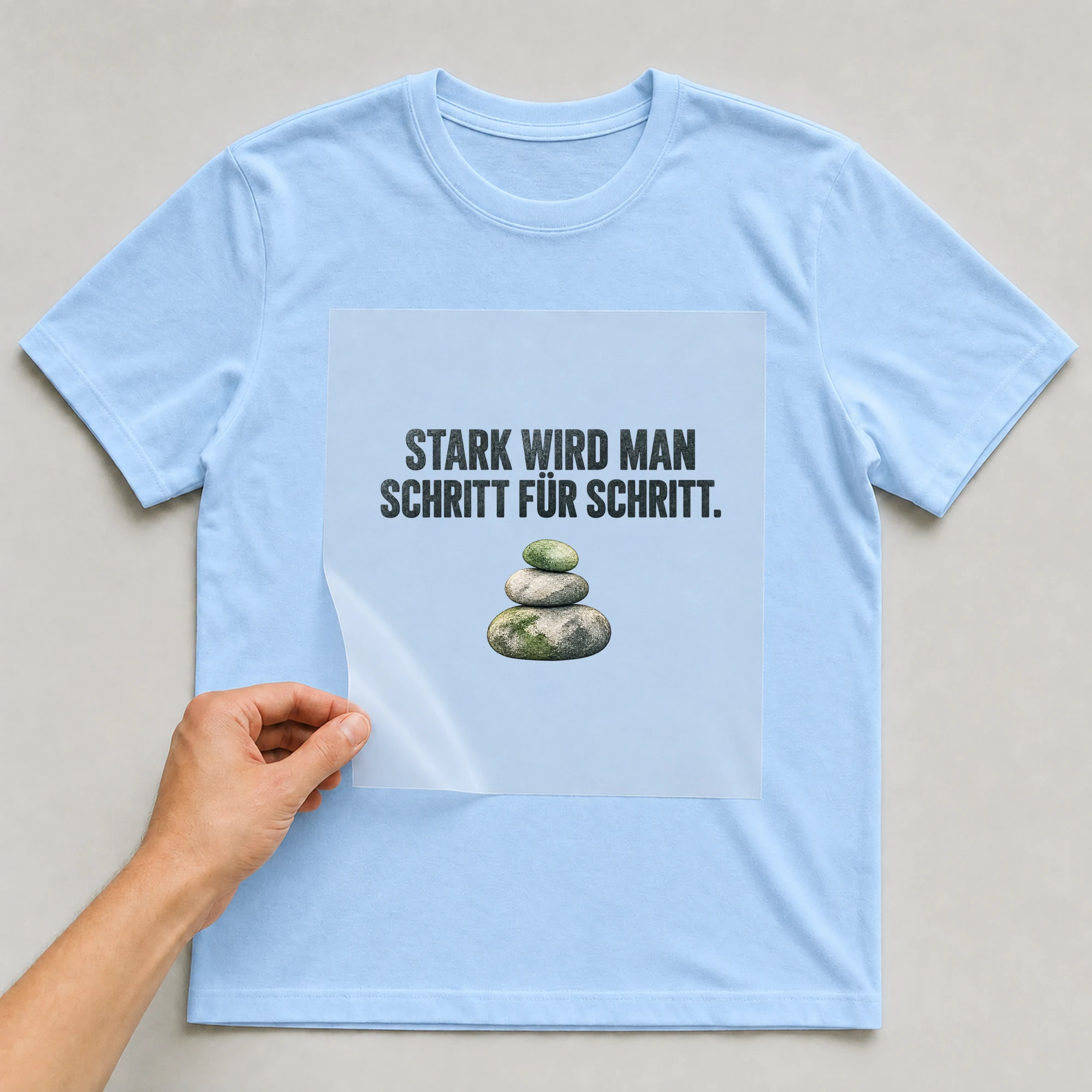 Bügelbild „STARK WIRD MAN SCHRITT FÜR SCHRITT.“ auf babyblauem T-Shirt, Folie wird aufgelegt