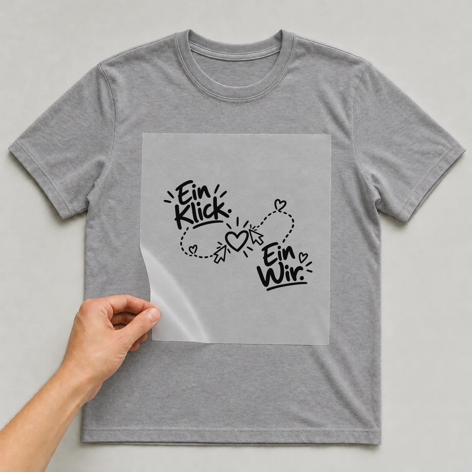 Bügelbild „Ein Klick. Ein Wir.“ auf grauem T-Shirt, Folie wird aufgelegt