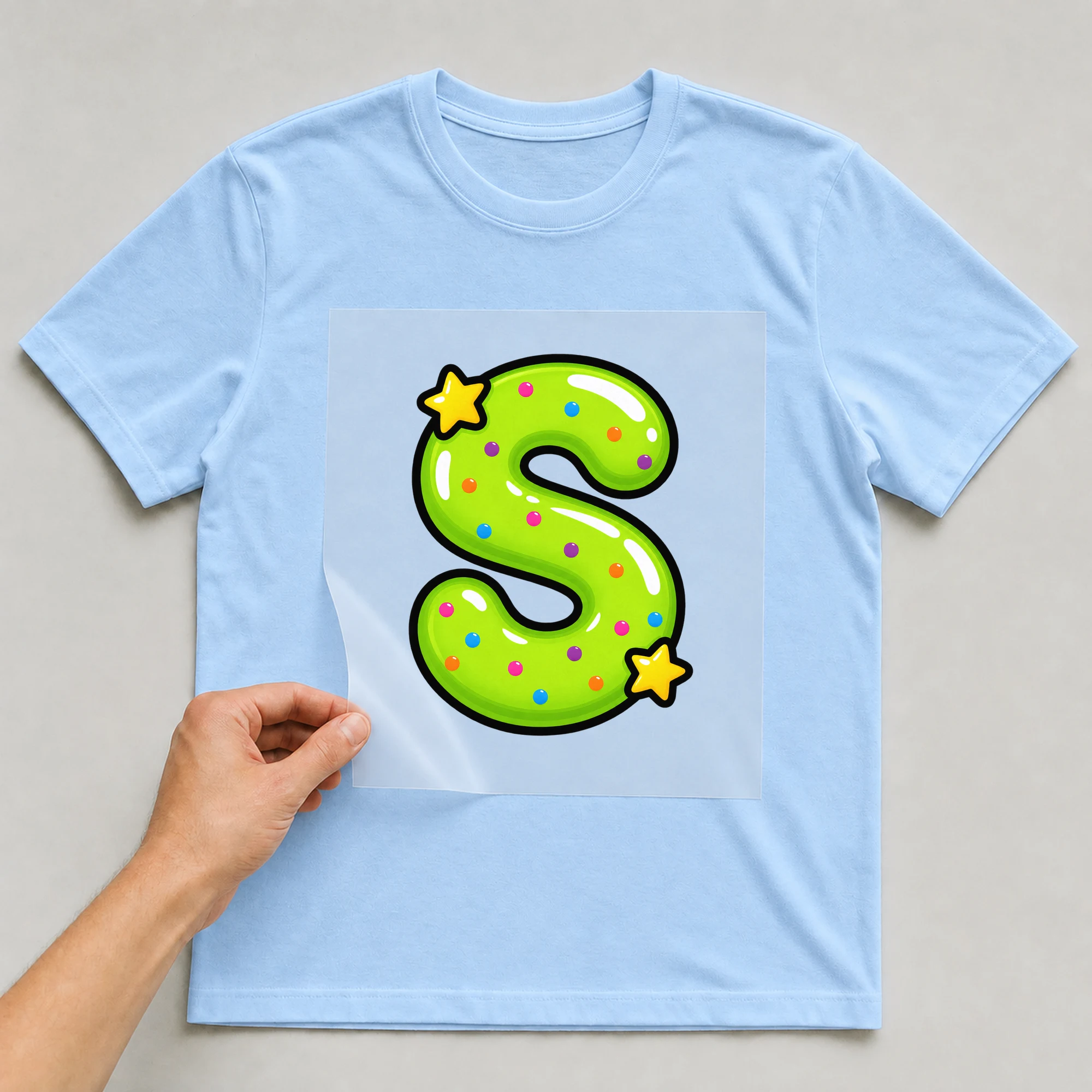 Bügelbild „Buchstabe S im Comic-Ballon-Stil“ auf babyblauem T-Shirt, Folie wird aufgelegt