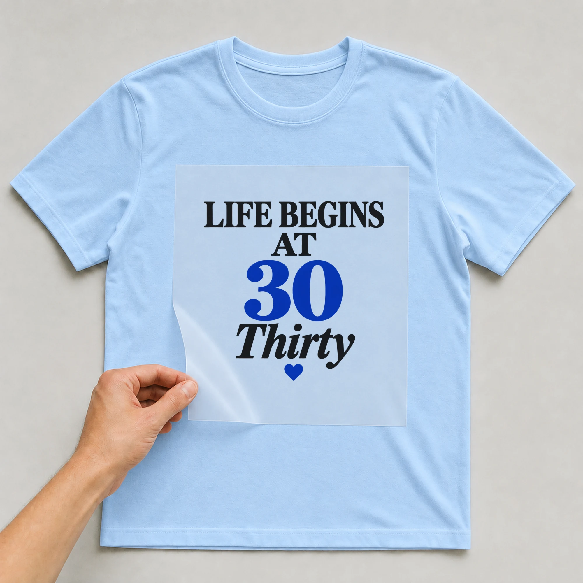 Bügelbild „Life Begins At 30 Thirty“ auf babyblauem T-Shirt, Folie wird aufgelegt