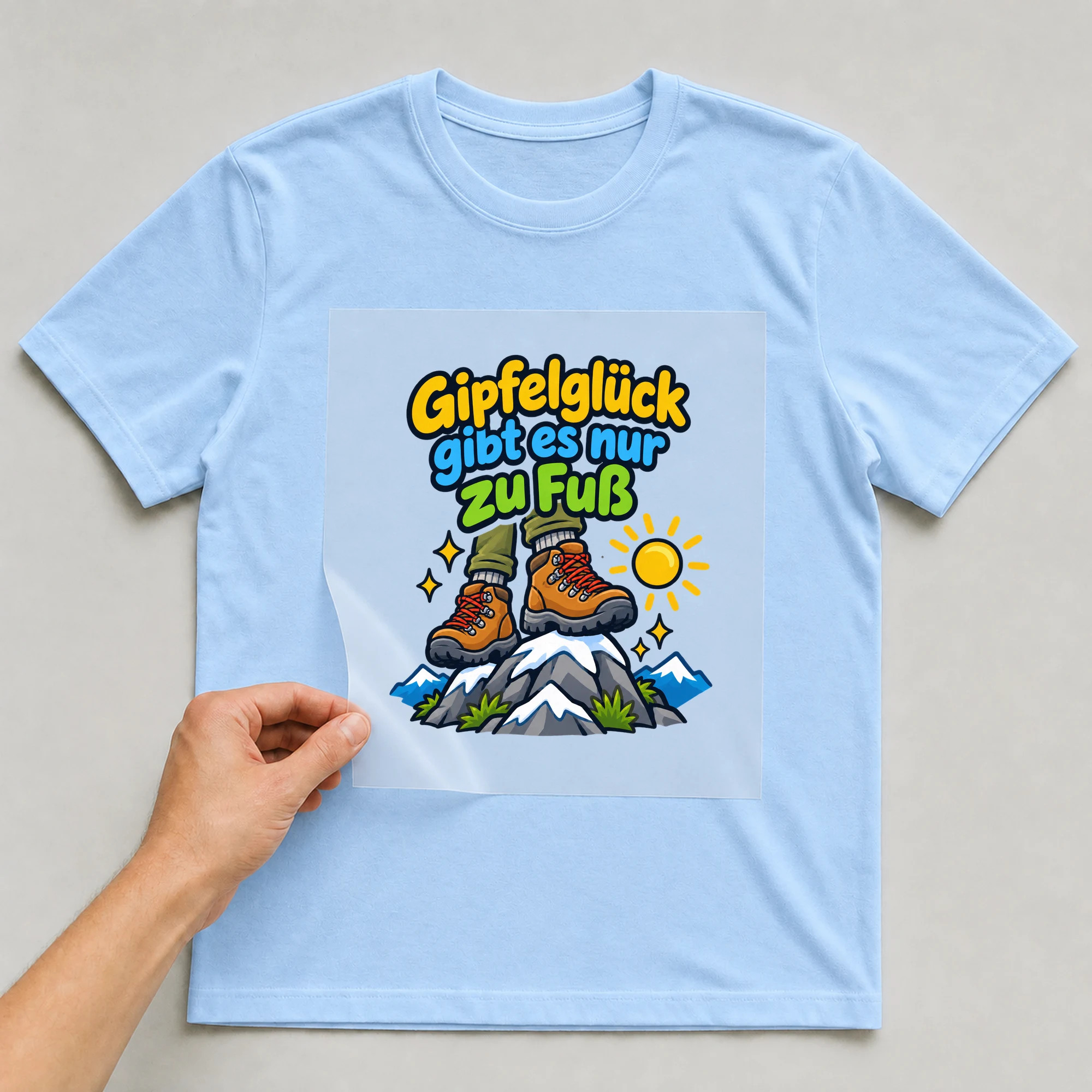 Bügelbild „Gipfelglück gibt es nur zu Fuß“ auf babyblauem T-Shirt, Folie wird aufgelegt