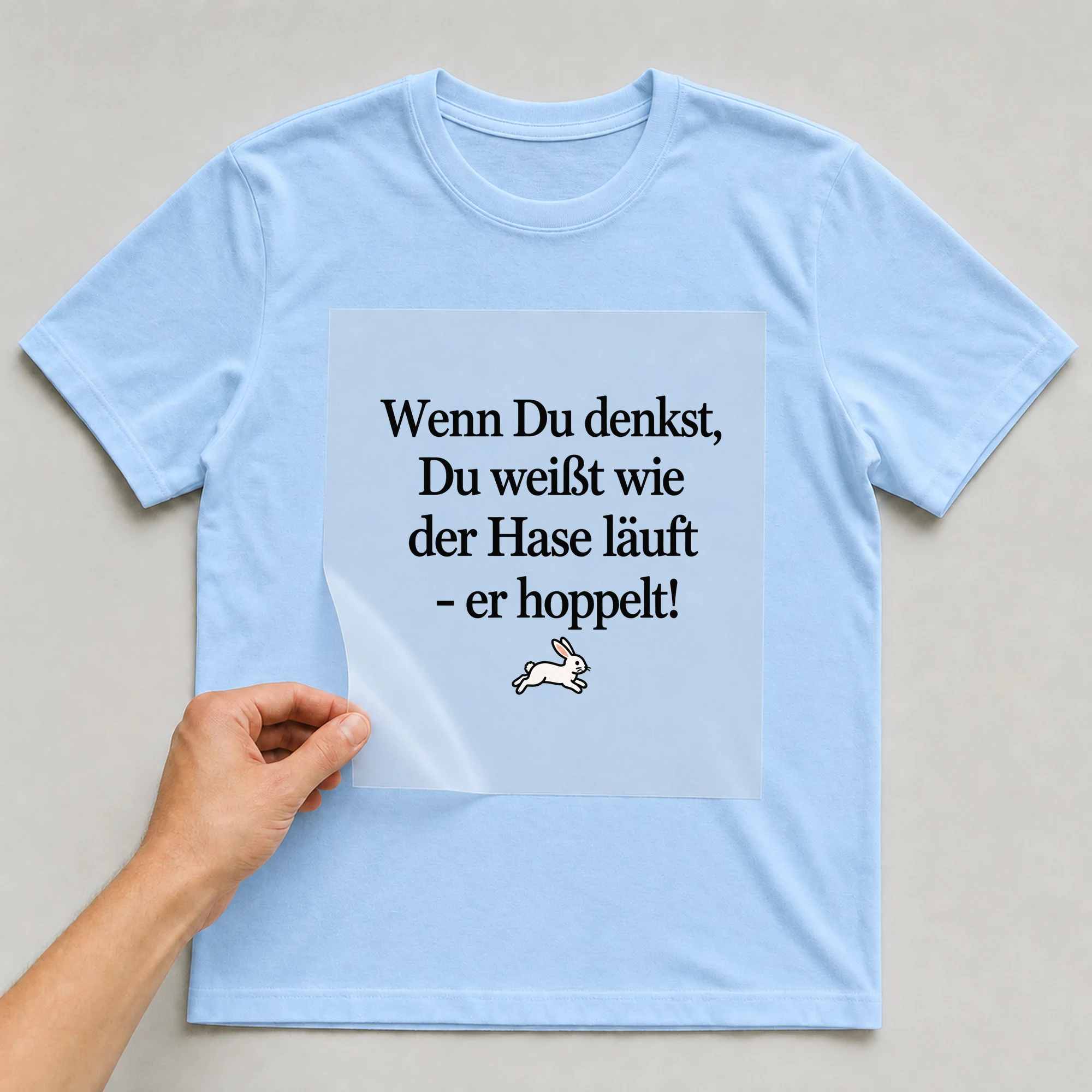 Bügelbild „Wenn Du denkst, Du weißt wie der Hase läuft - er hoppelt!“ auf babyblauem T-Shirt, Folie wird aufgelegt