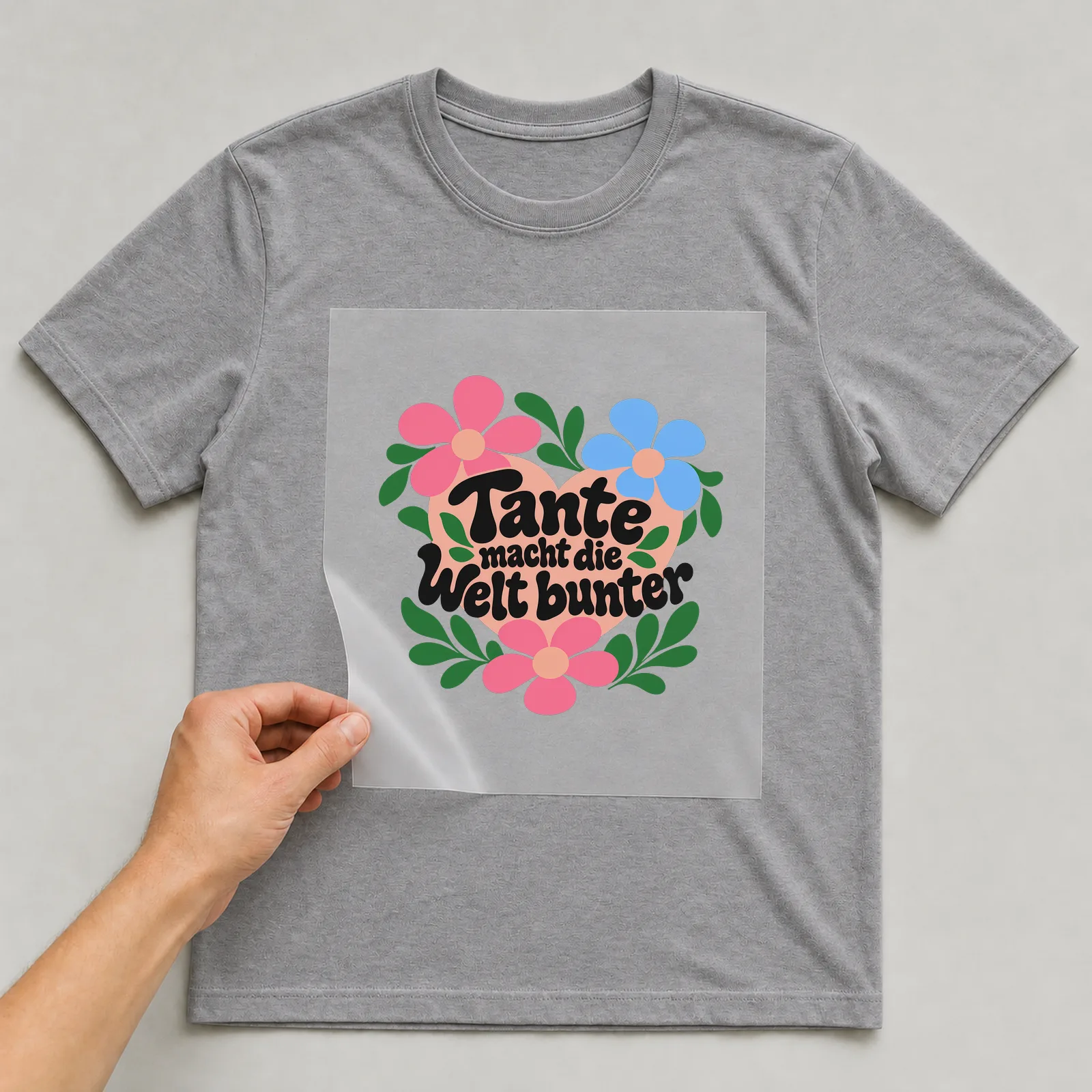 Bügelbild „Tante macht die Welt bunter“ auf grauem T-Shirt, Folie wird aufgelegt