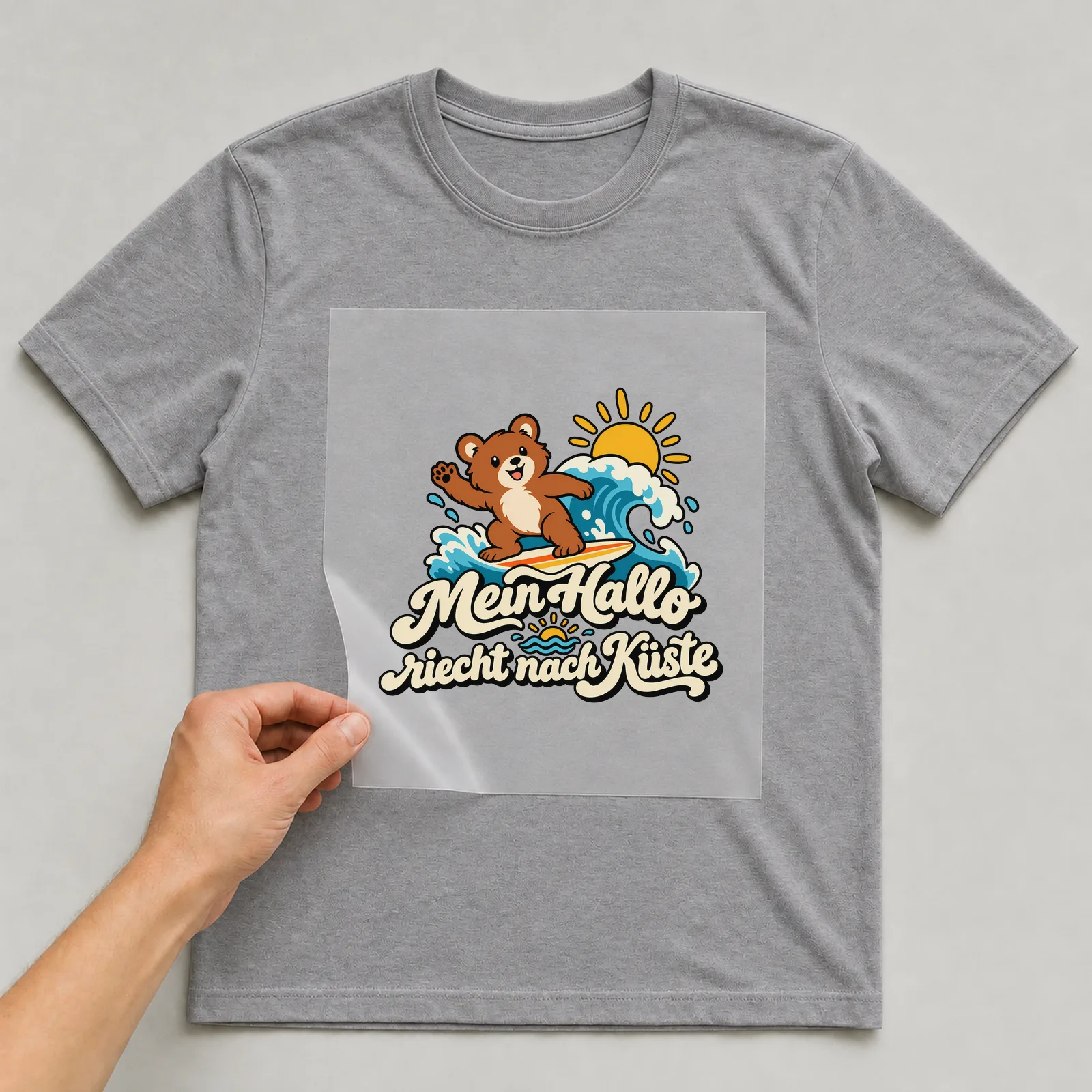 Bügelbild „Mein Hallo riecht nach Küste“ auf grauem T-Shirt, Folie wird aufgelegt