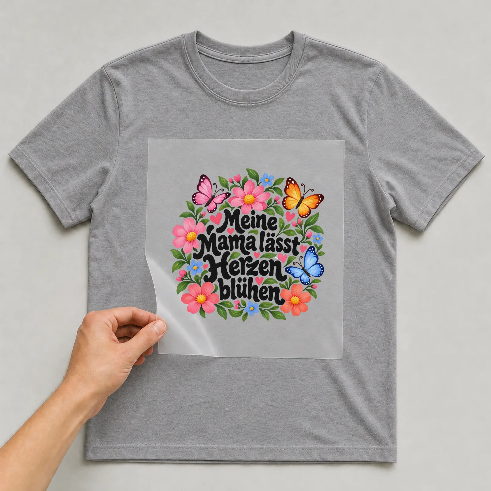 Bügelbild „Meine Mama lässt Herzen blühen“ auf grauem T-Shirt, Folie wird aufgelegt