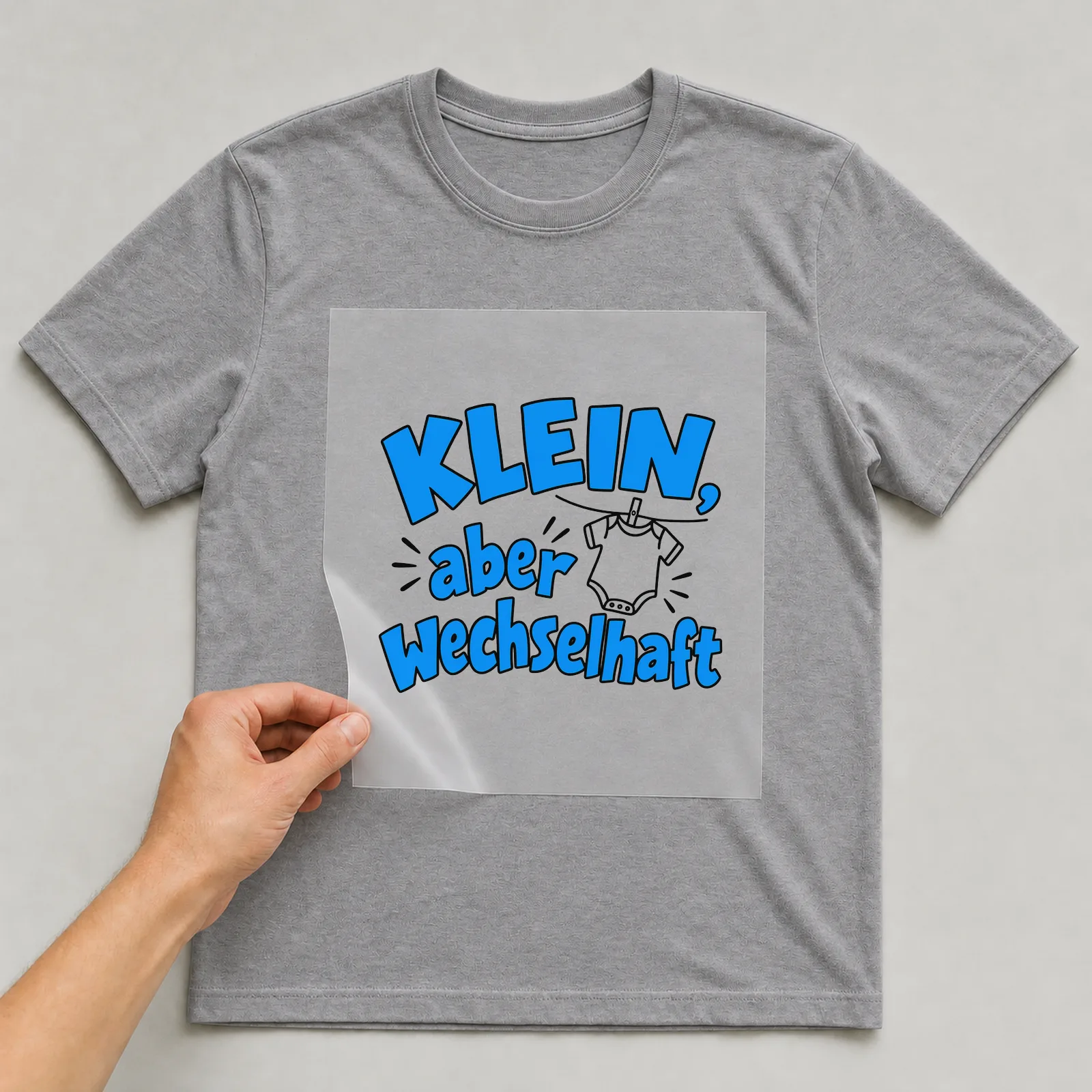 Bügelbild „Klein, aber wechselhaft“ auf grauem T-Shirt, Folie wird aufgelegt