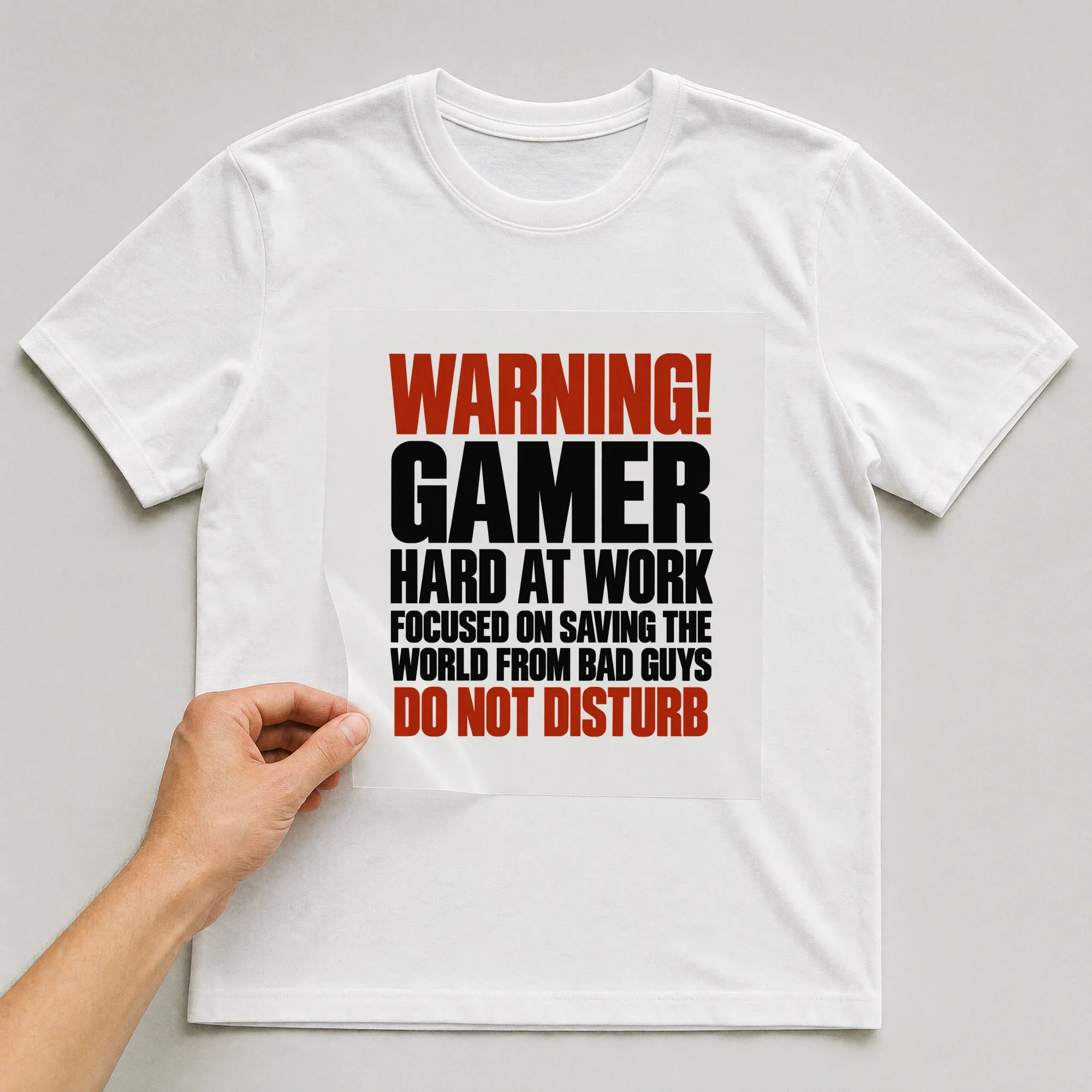Bügelbild „Warning! Gamer Hard At Work Focused On Saving The World From Bad Guys Do Not“ auf weißem T-Shirt, Folie wird aufgelegt