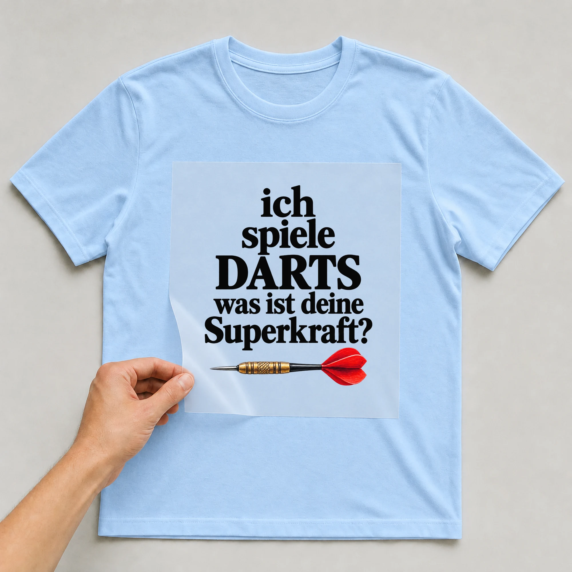 Bügelbild „ich spiele DARTS was ist deine Superkraft?“ auf babyblauem T-Shirt, Folie wird aufgelegt