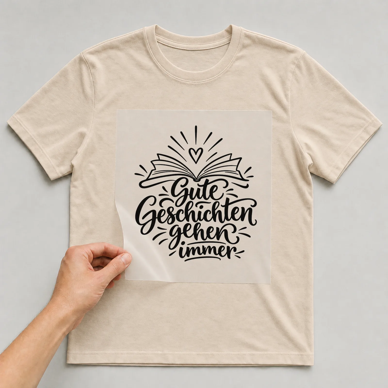 Bügelbild „Gute Geschichten gehen immer“ auf beigem T-Shirt, Folie wird aufgelegt