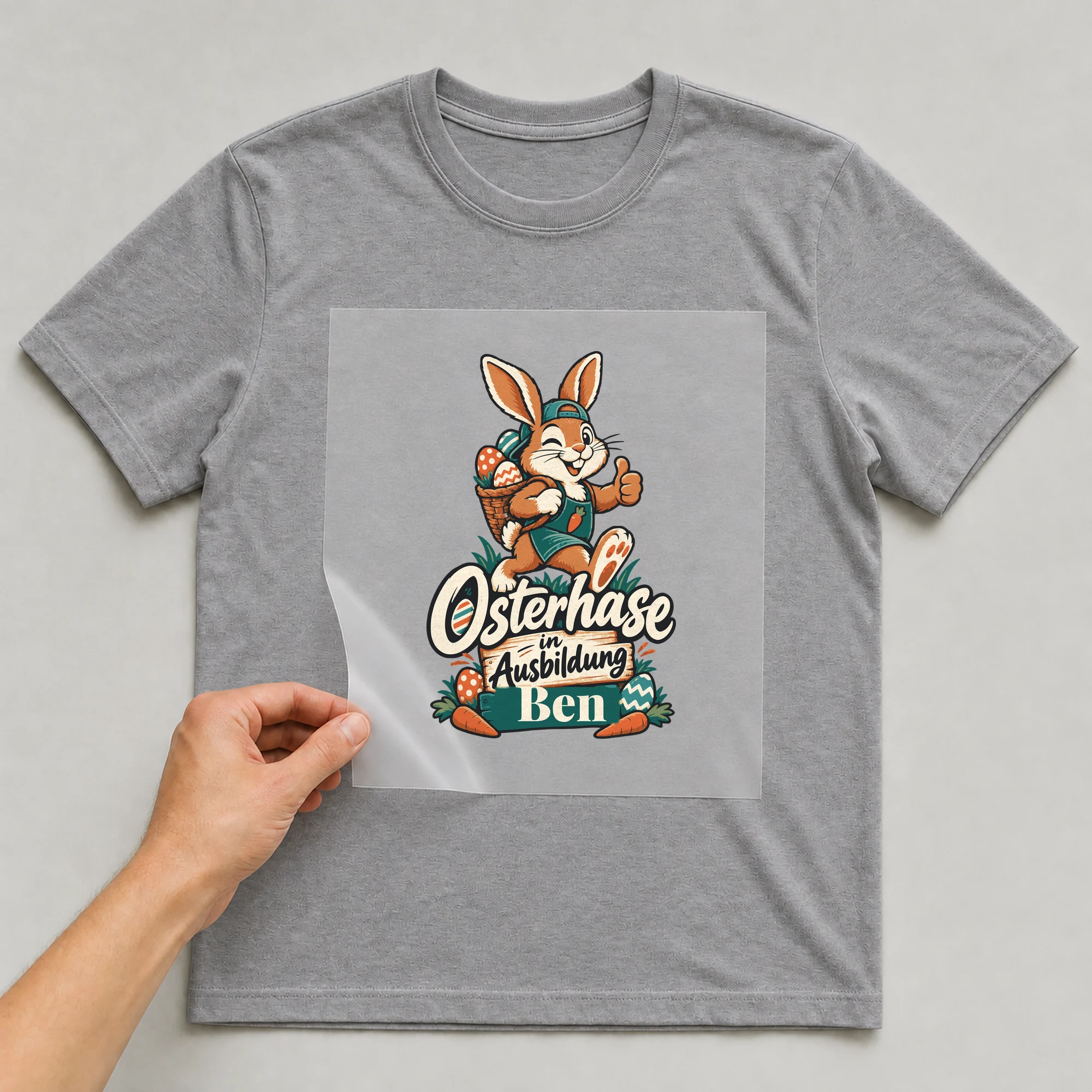 Bügelbild Osterhase in Ausbildung mit Name auf grauem T-Shirt, Folie wird aufgelegt