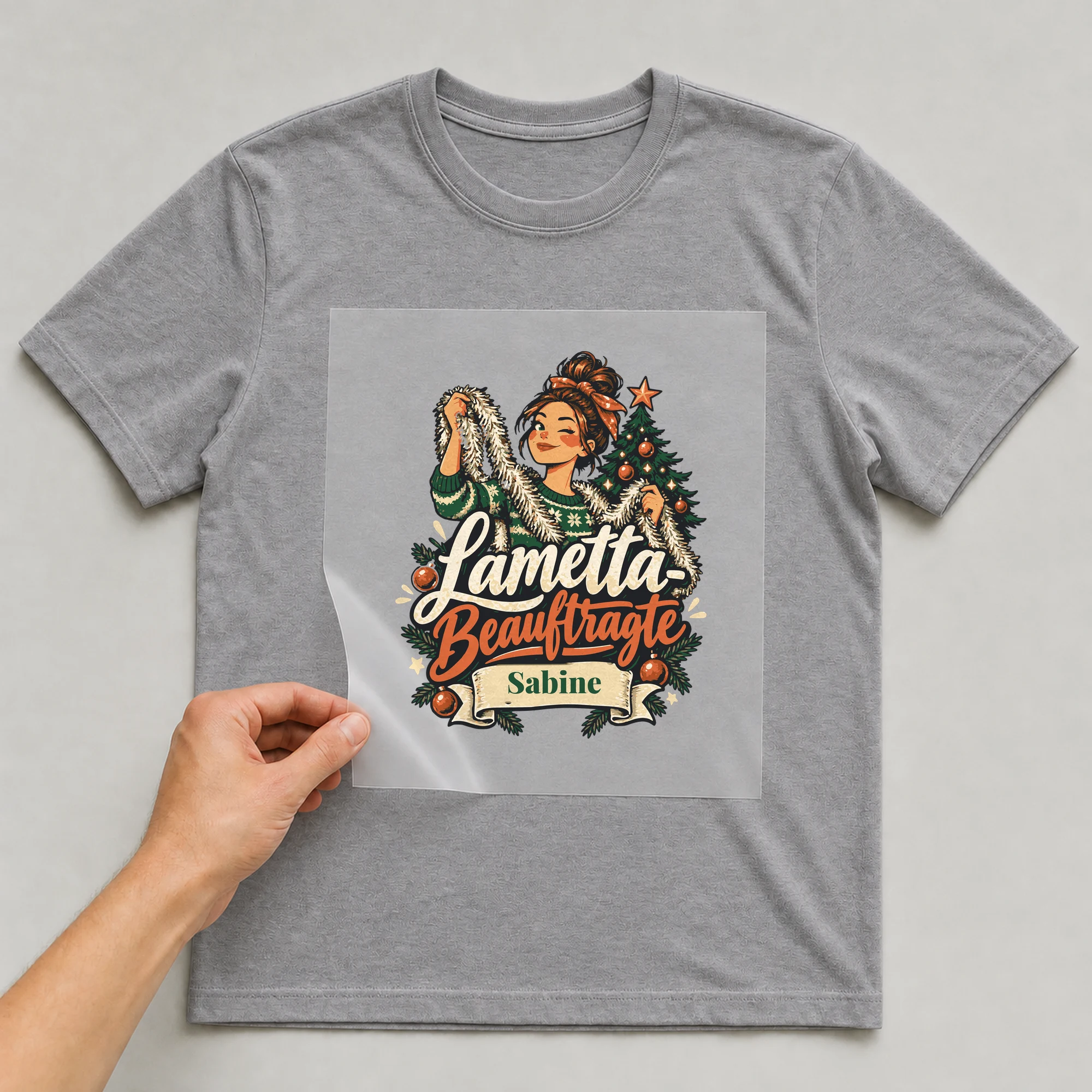 Bügelbild Lametta-Beauftragte mit Name auf grauem T-Shirt, Folie wird aufgelegt