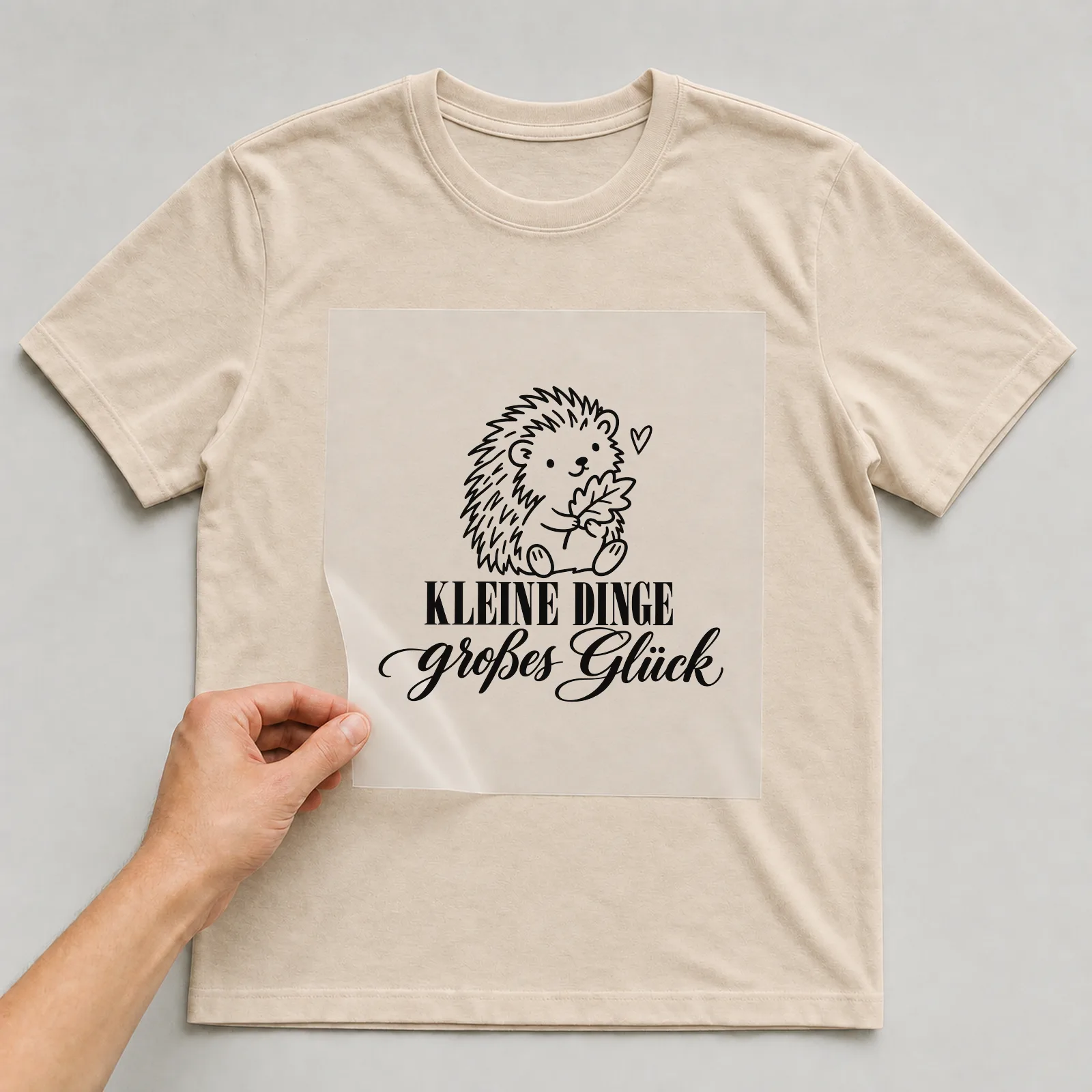 Bügelbild „Kleine Dinge großes Glück“ auf beigem T-Shirt, Folie wird aufgelegt