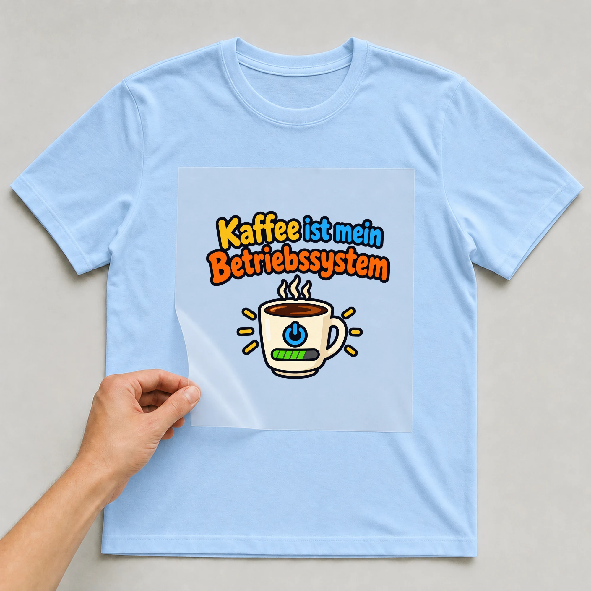 Bügelbild „Kaffee ist mein Betriebssystem“ auf babyblauem T-Shirt, Folie wird aufgelegt