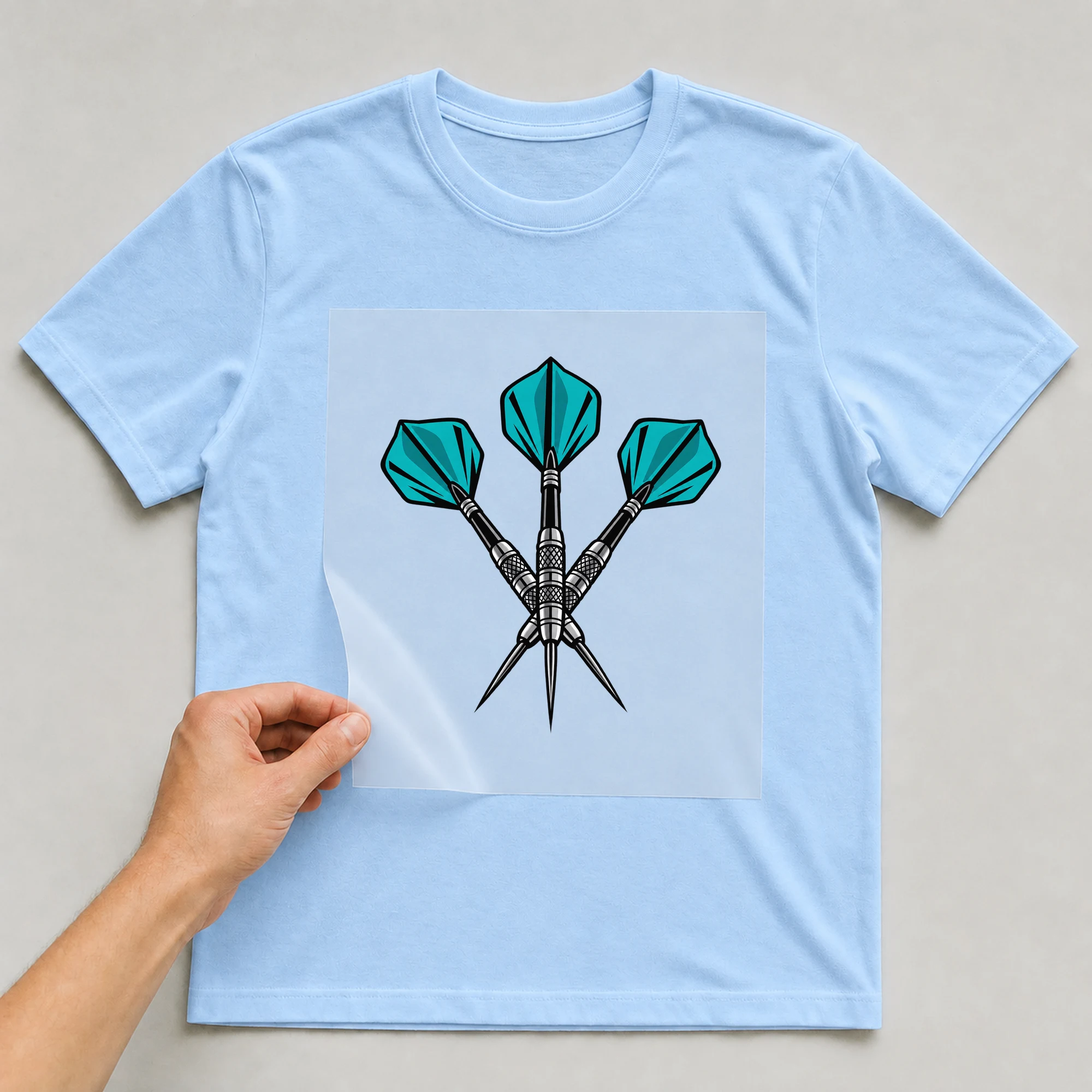 Bügelbild „Dartpfeile“ auf babyblauem T-Shirt, Folie wird aufgelegt