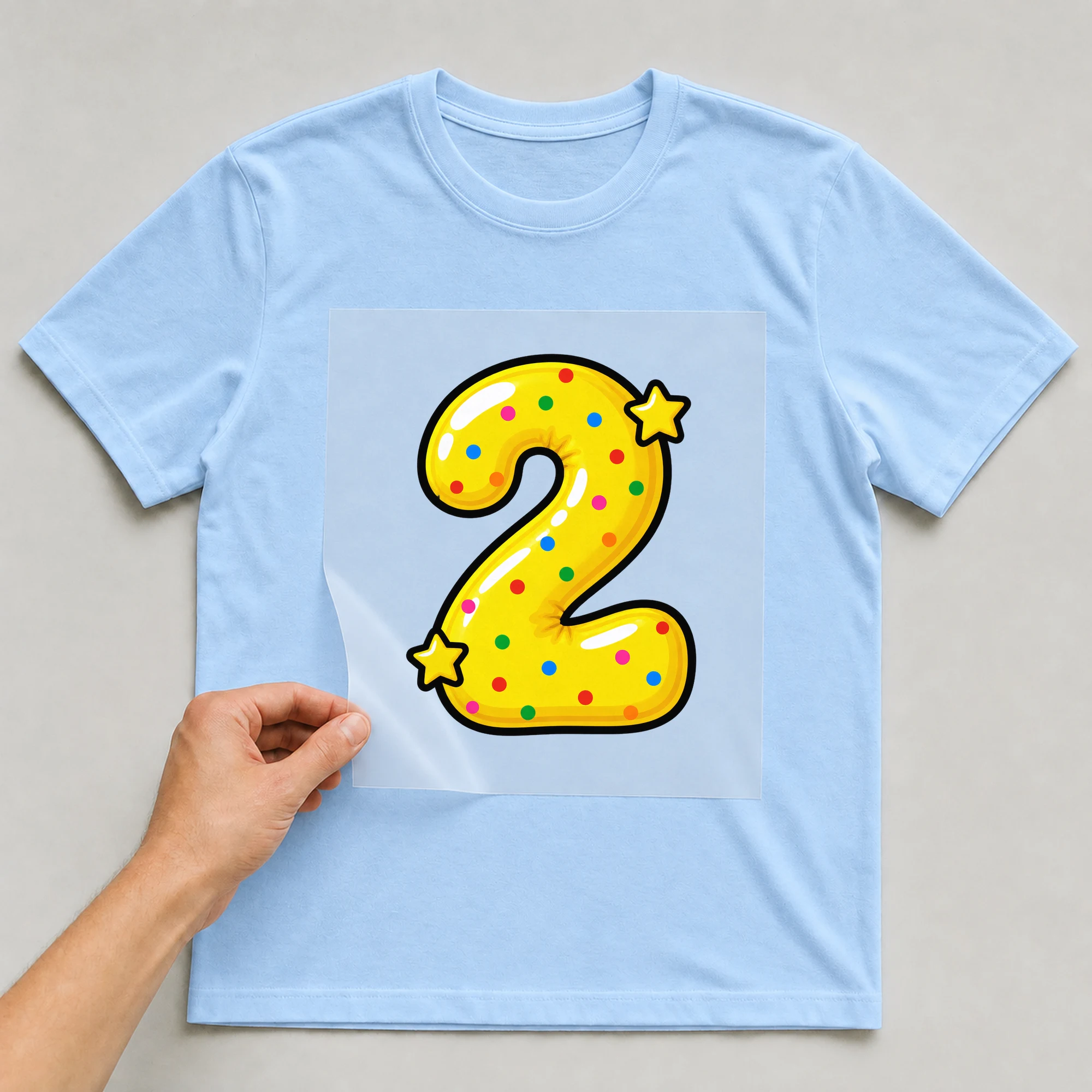 Bügelbild „Zahl 2 im Comic-Ballon-Stil“ auf babyblauem T-Shirt, Folie wird aufgelegt