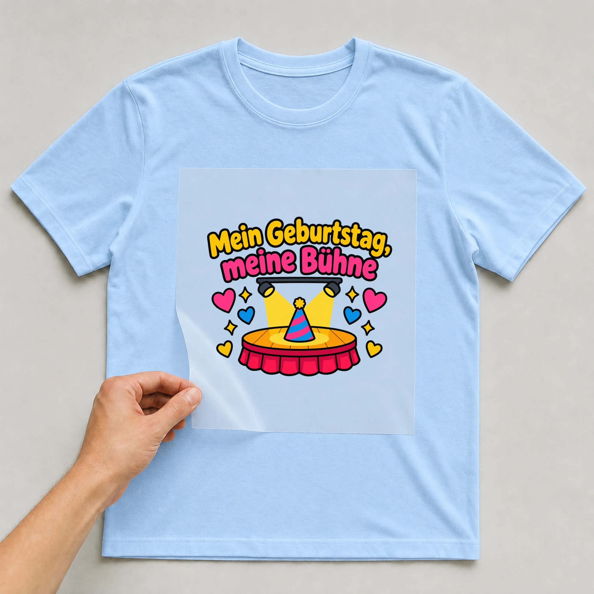 Bügelbild „Mein Geburtstag, meine Bühne“ auf babyblauem T-Shirt, Folie wird aufgelegt