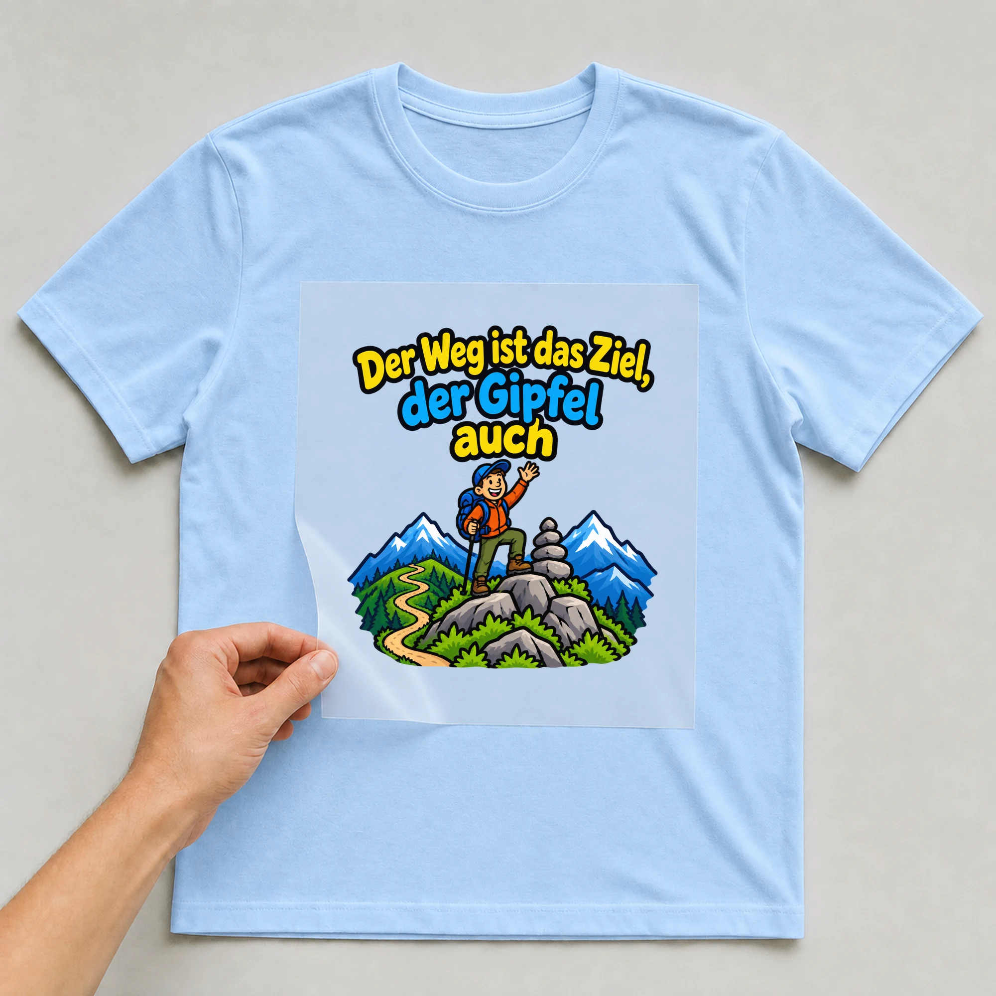 Bügelbild „Der Weg ist das Ziel, der Gipfel auch“ auf babyblauem T-Shirt, Folie wird aufgelegt