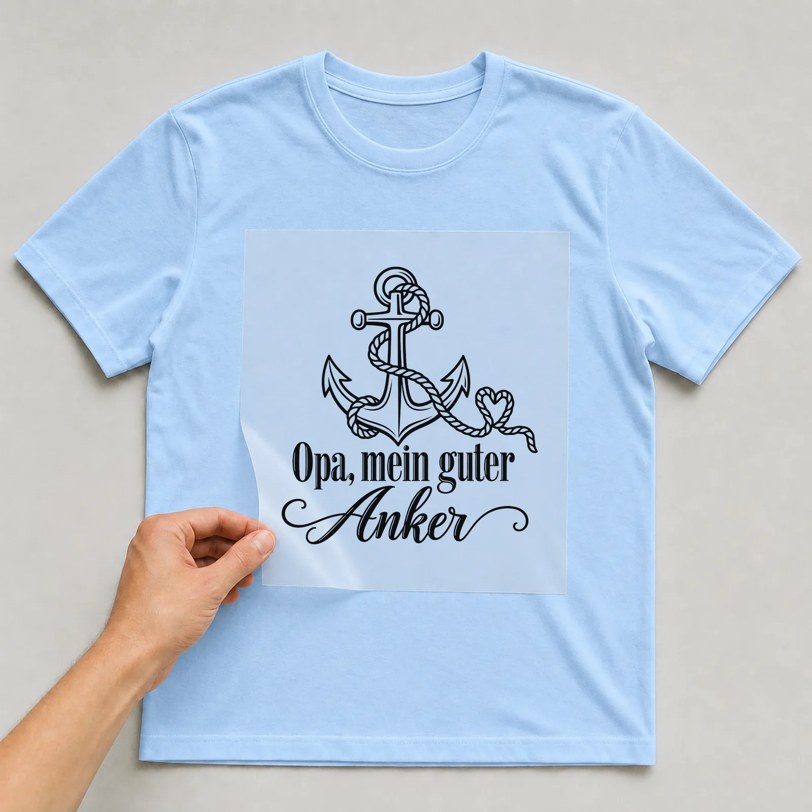 Bügelbild „Opa, mein guter Anker“ auf hellblauem T-Shirt, Folie wird aufgelegt