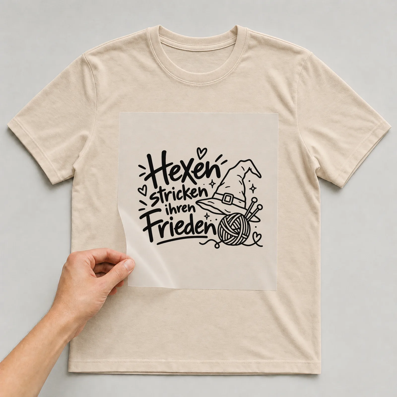 Bügelbild „Hexen stricken ihren Frieden“ auf beigem T-Shirt, Folie wird aufgelegt